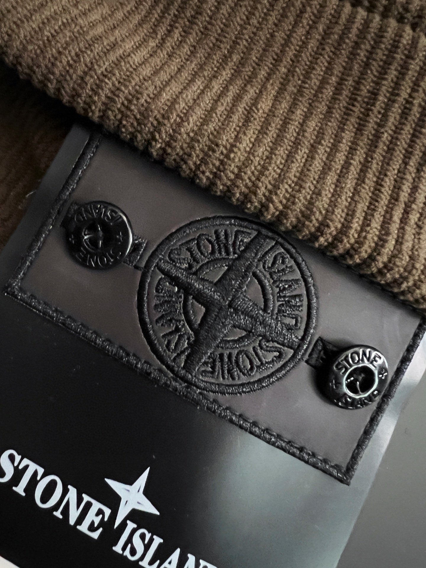 Embossed Stone Island logo leather patch on textured brown fabric