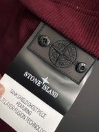 Stone Island logo patch on burgundy pants near care label