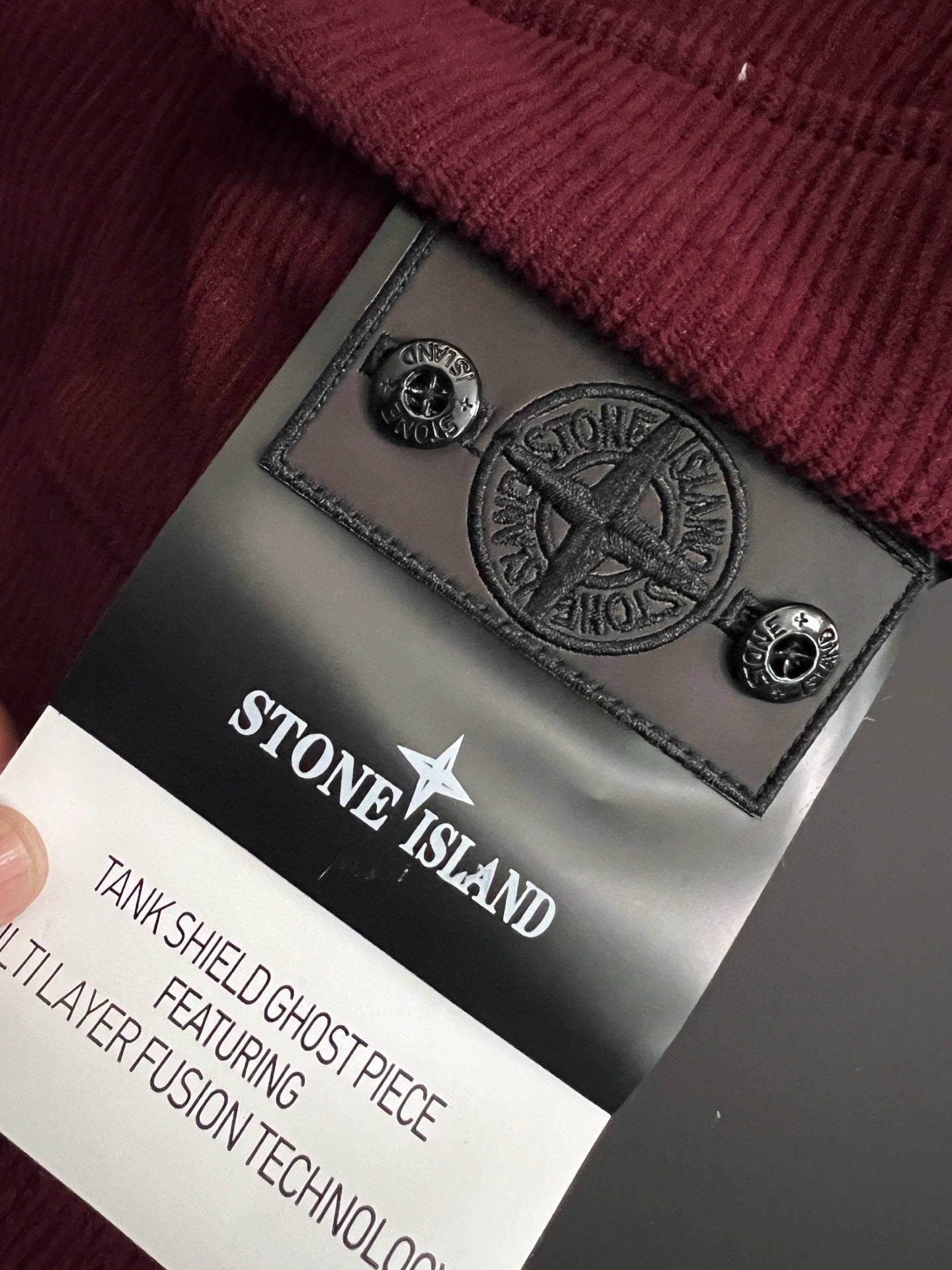Stone Island logo patch on burgundy pants near care label