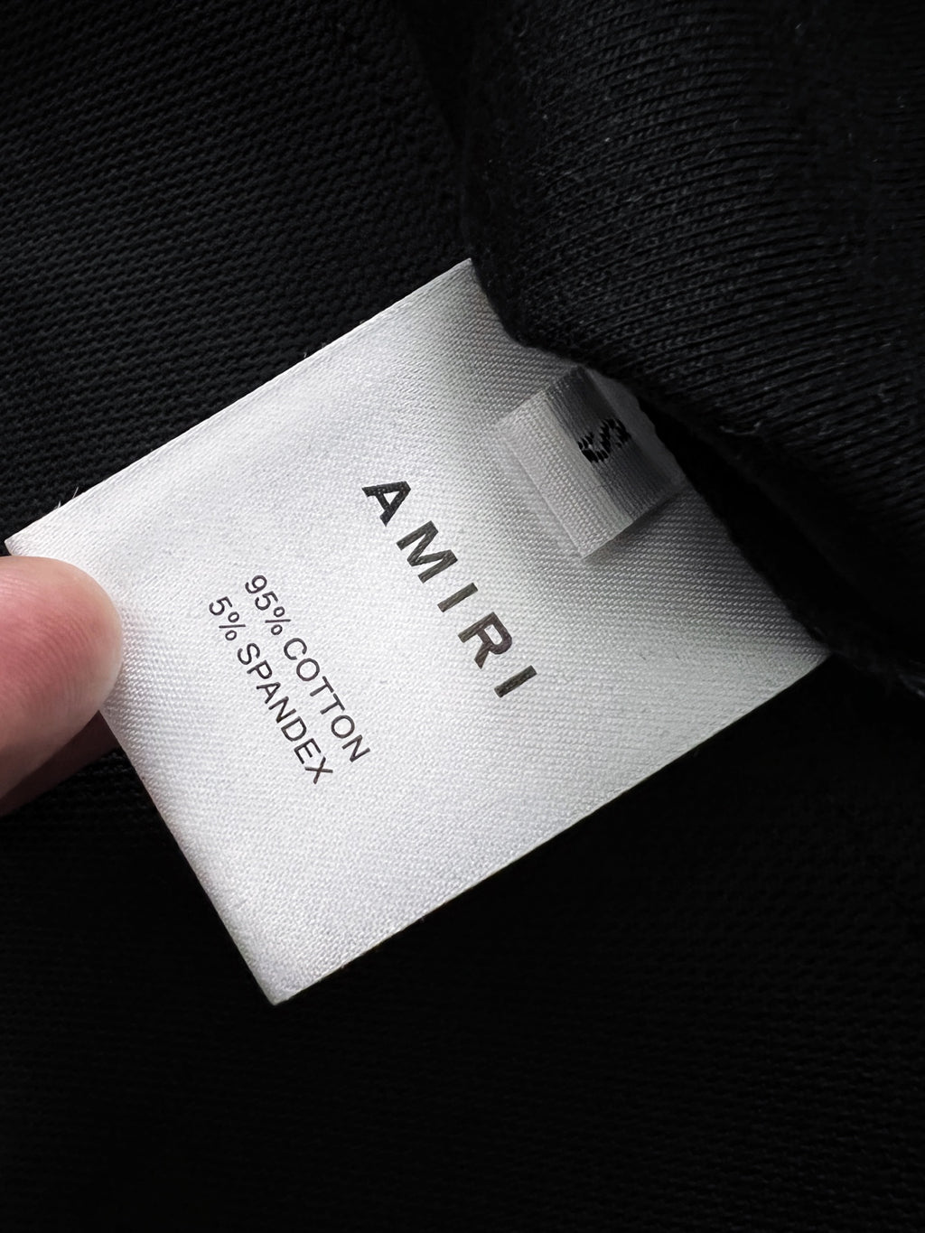 White care label reading AMIRI and 100% cotton on black fabric