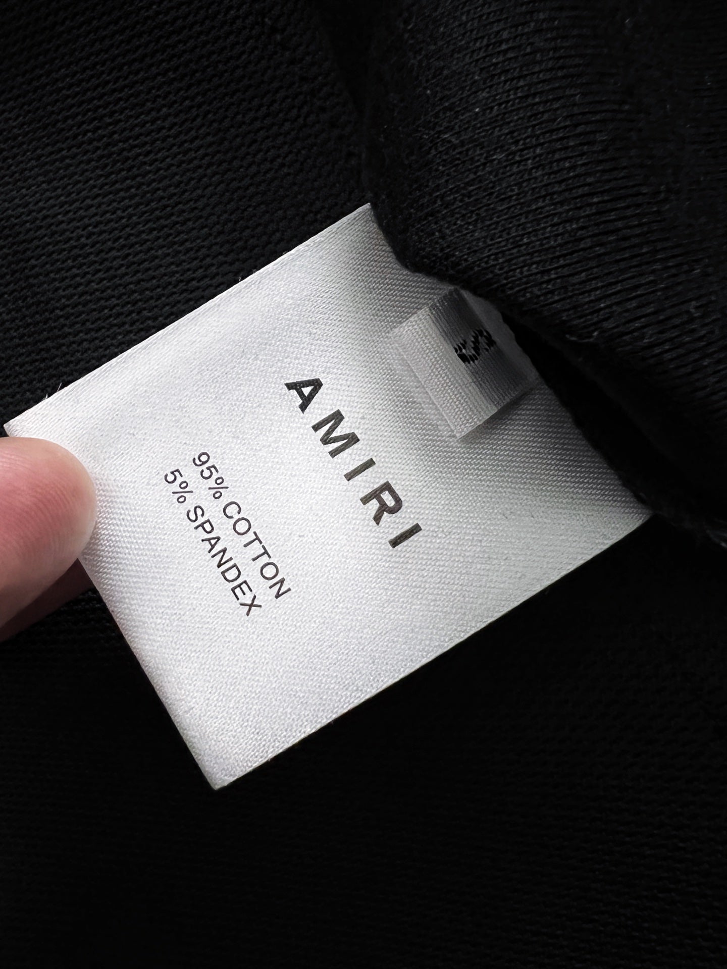 White care label reading AMIRI and 100% cotton on black fabric