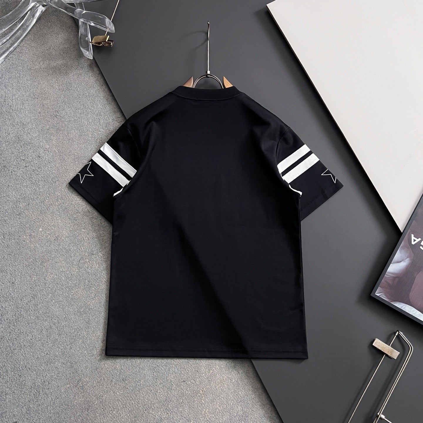 Black T-shirt with striped sleeve cuffs, shown from the back on a hanger