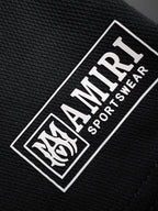 Black woven label reading AMIRI SPORTWEAR with horse graphic border