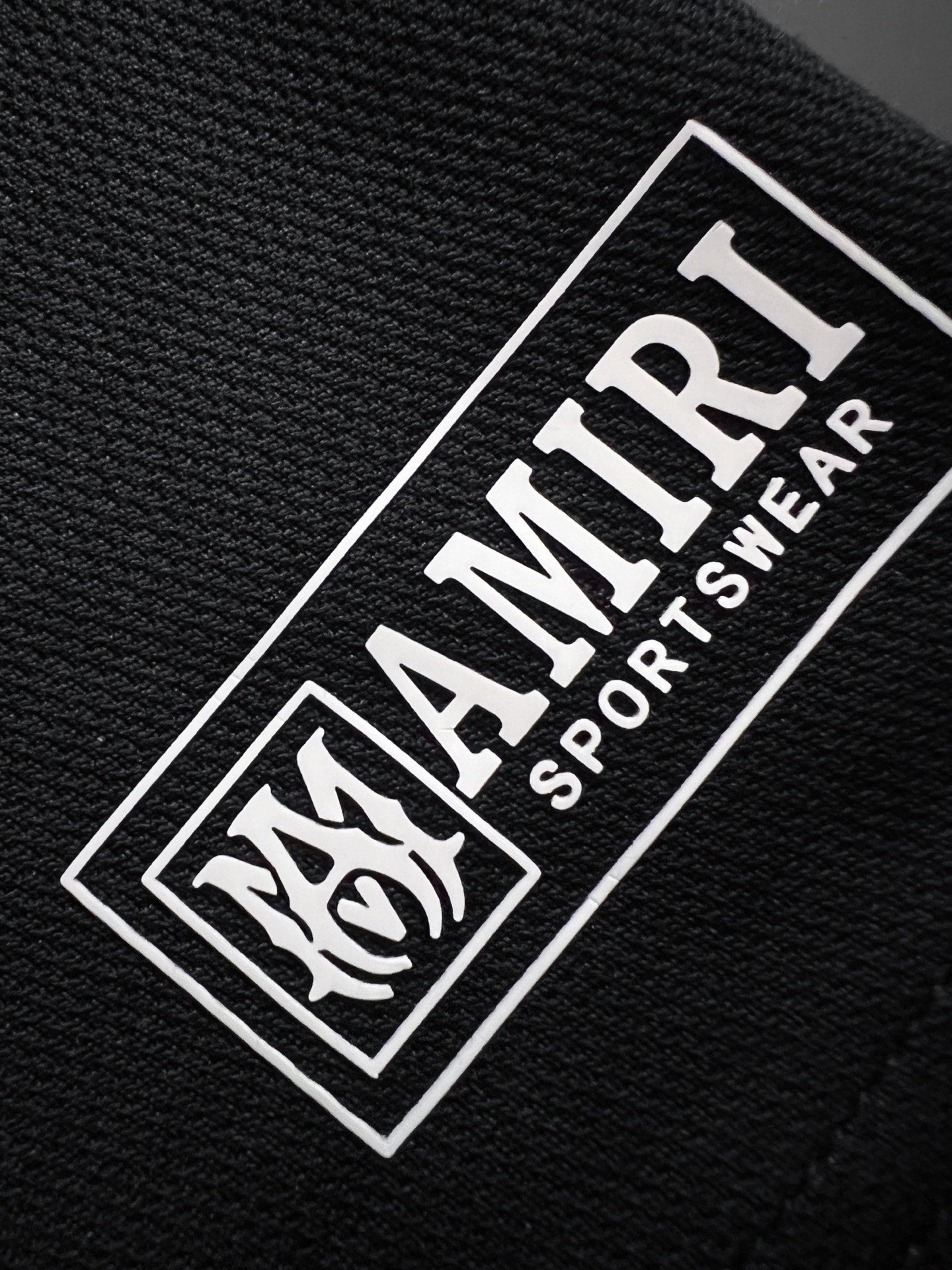 Black woven label reading AMIRI SPORTWEAR with horse graphic border