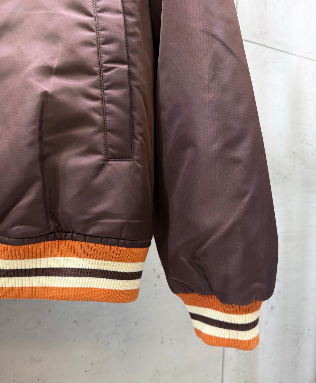Burgundy bomber jacket with orange, white, and black striped ribbed sleeve cuffs