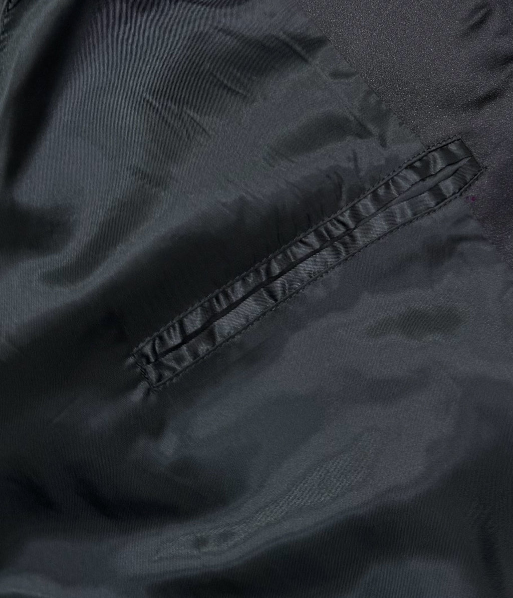 Black bomber jacket close-up showing stitched pocket panel and fabric texture