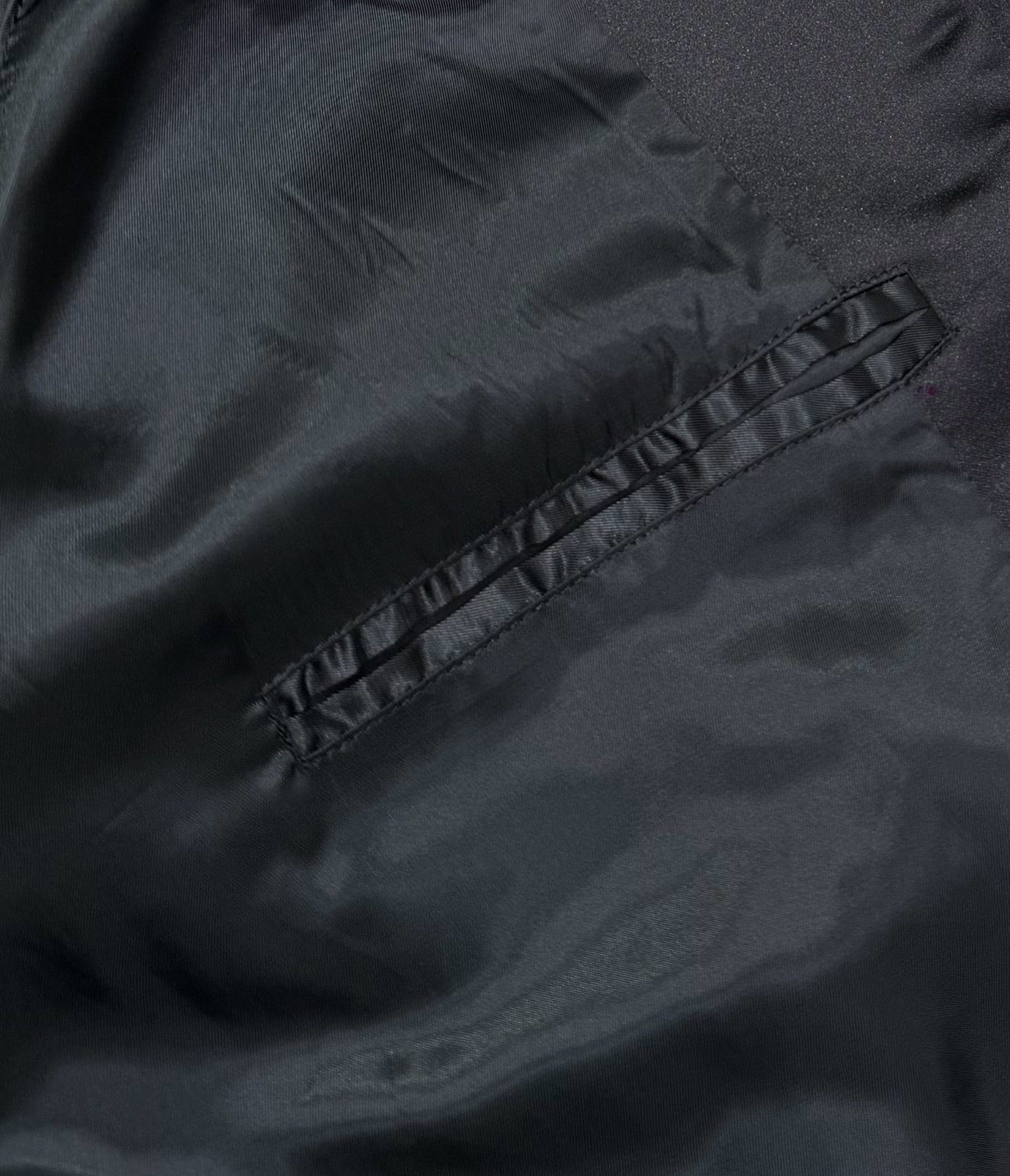 Black bomber jacket close-up showing stitched pocket panel and fabric texture