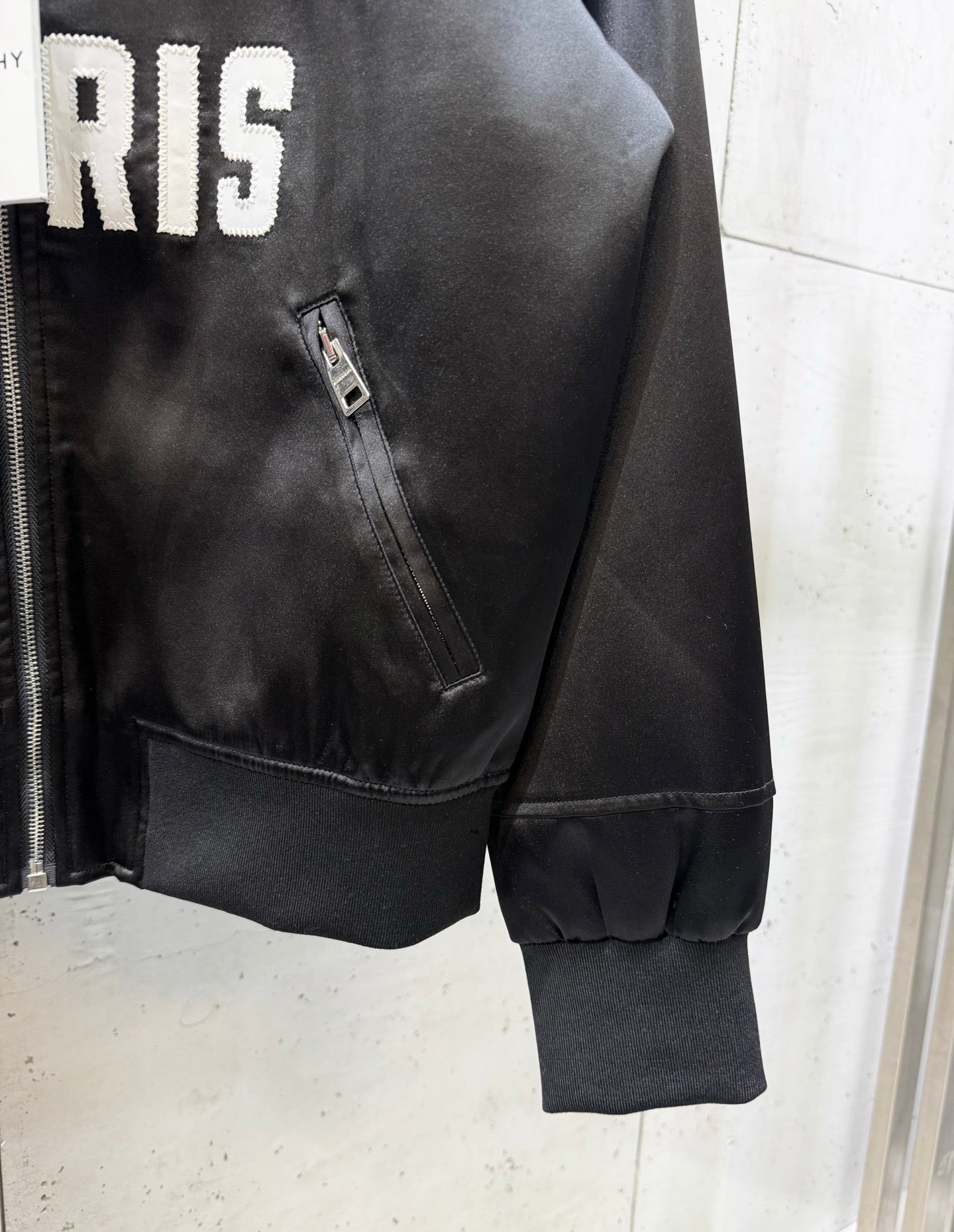 Black bomber jacket side view with diagonal zip pocket and ribbed sleeve cuff