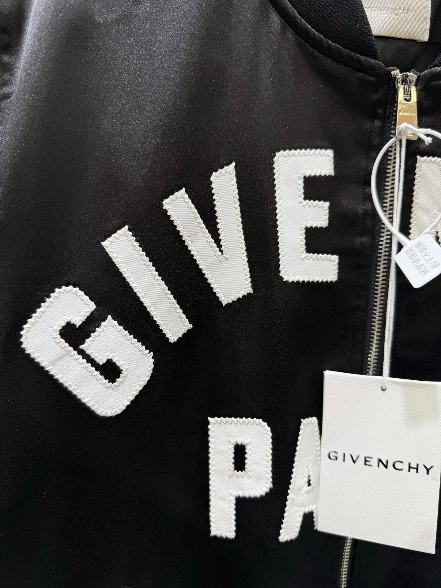 Black bomber jacket close-up with “GIVE…” and “PARIS” logo text