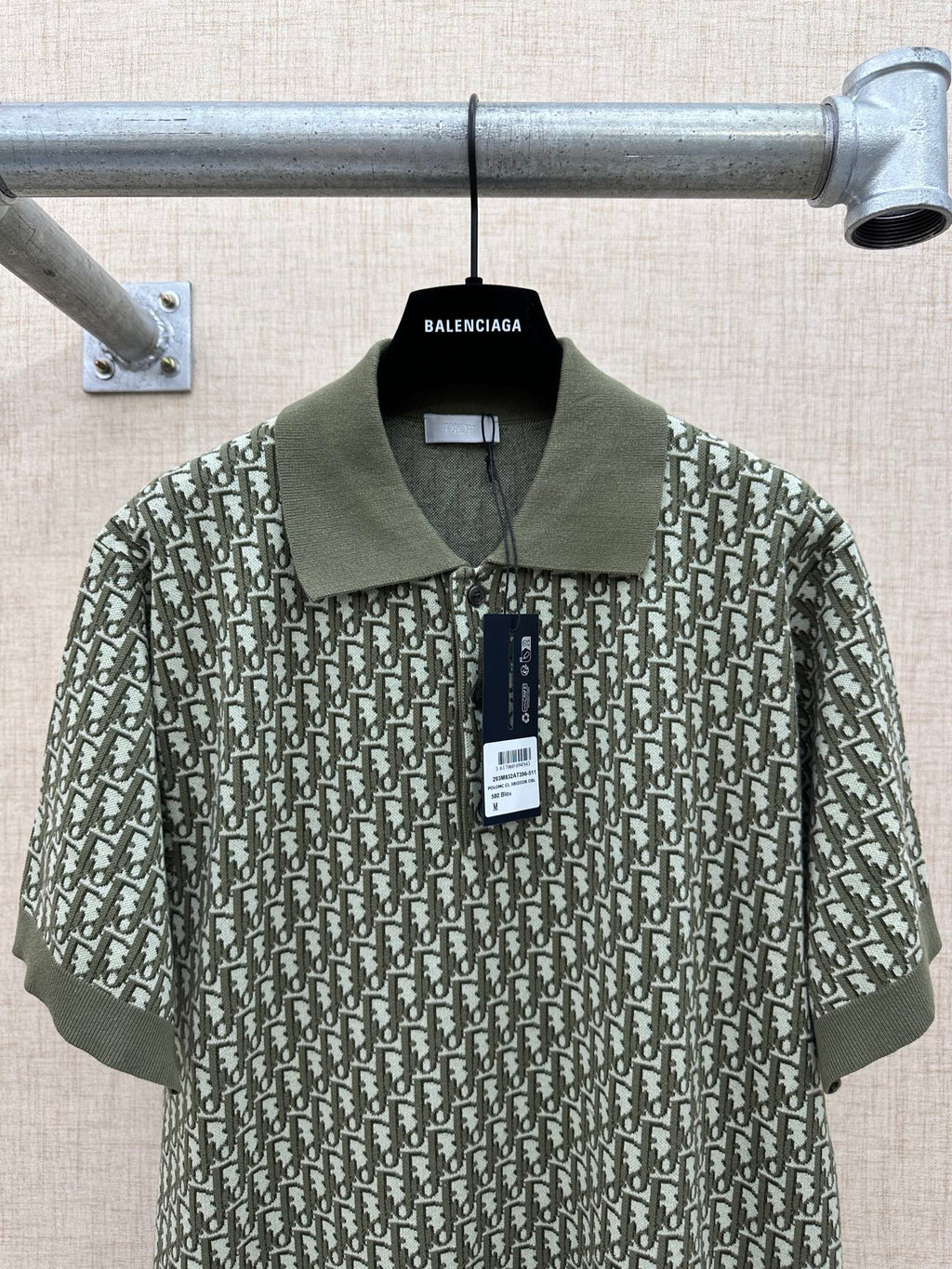 Dark green short-sleeve polo shirt with large repeat print and attached tag