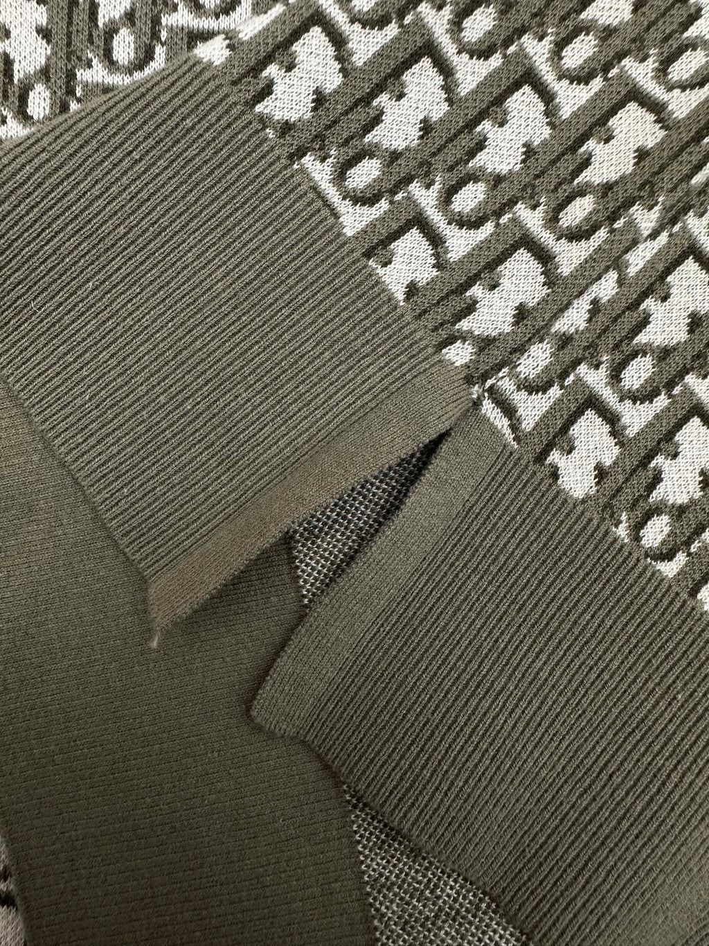 Dark green polo knit close-up with ribbed cuff and logo repeat fabric