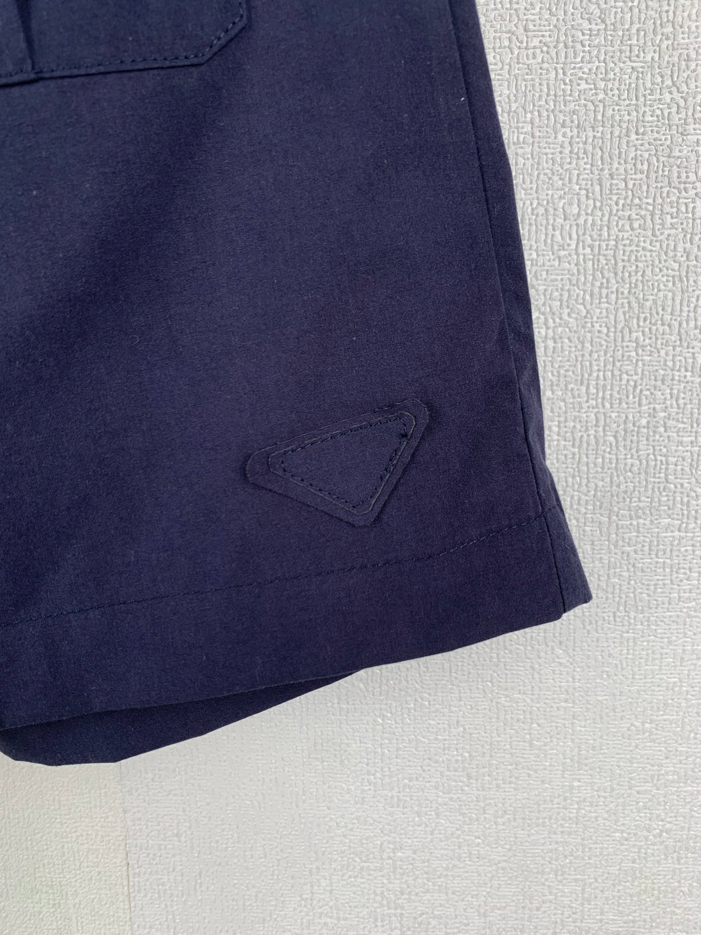 Navy Prada shorts with stitched triangular patch at the hem
