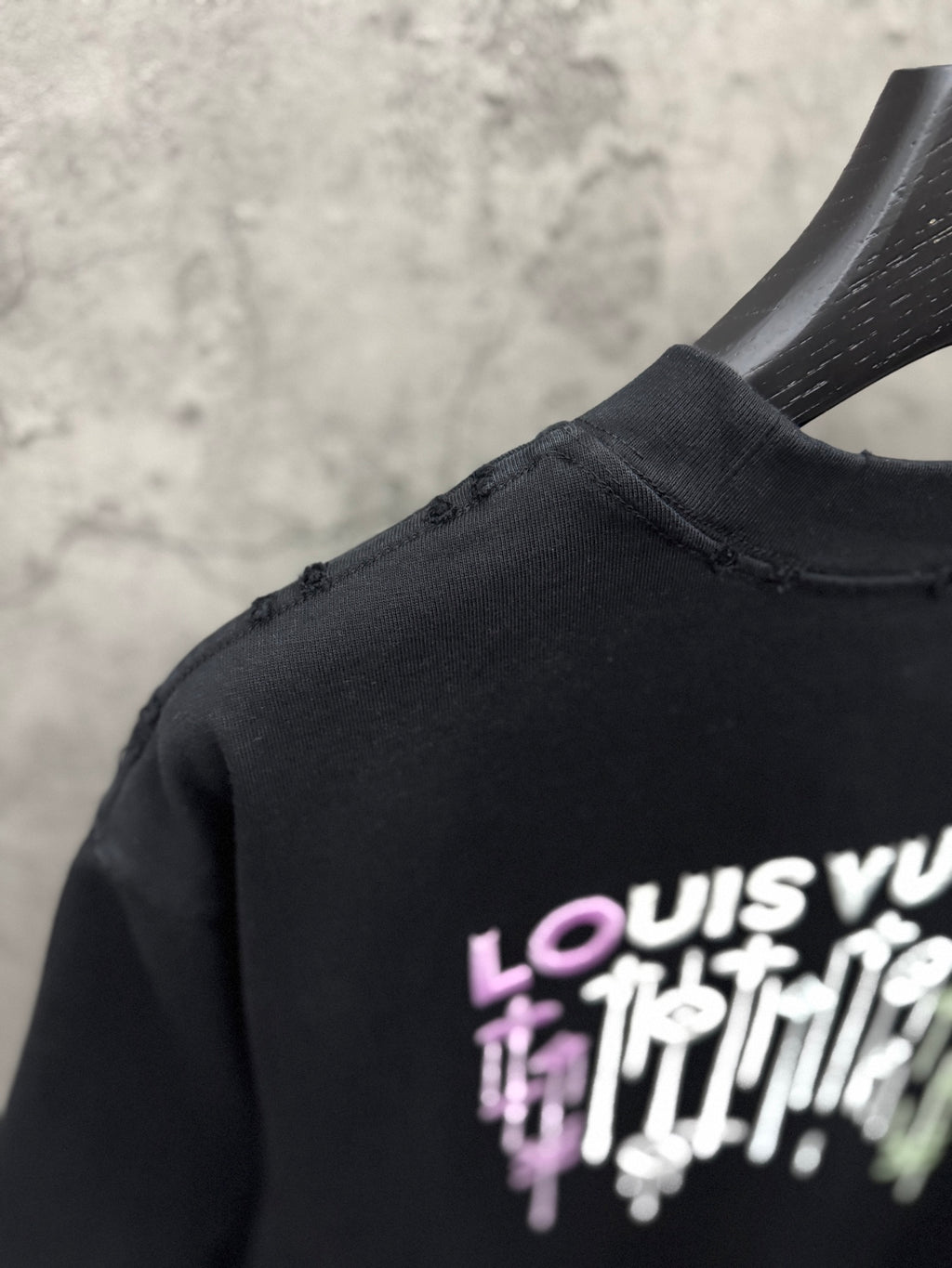 Black T-shirt shoulder with partial LOUIS VUITTON drip graphic