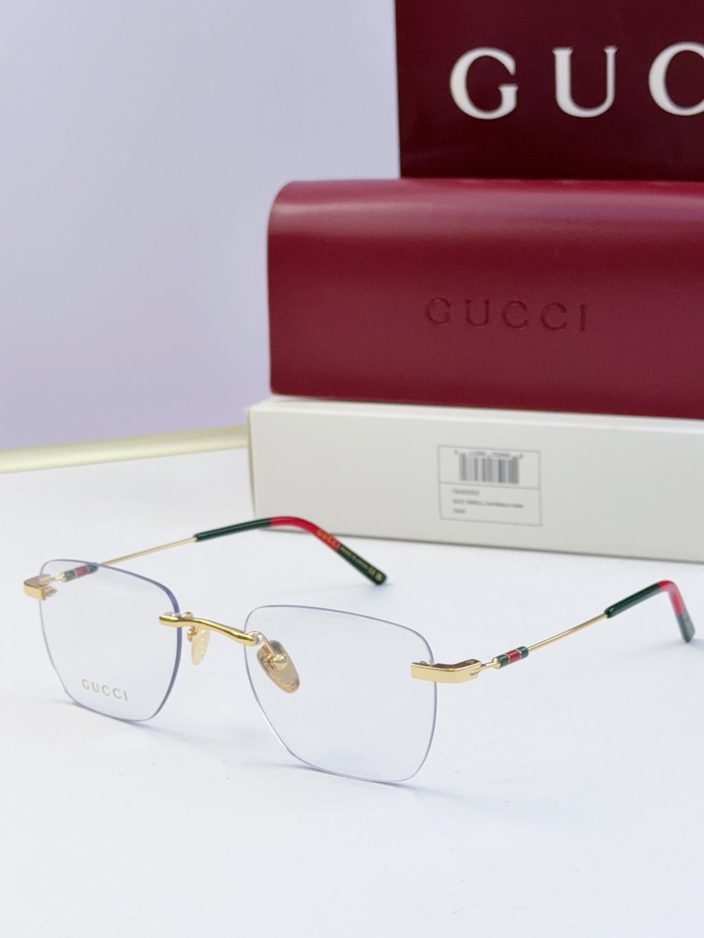Gucci eyeglasses with clear lenses, gold-tone metal frame, black temples with multicolor stripe and red accent