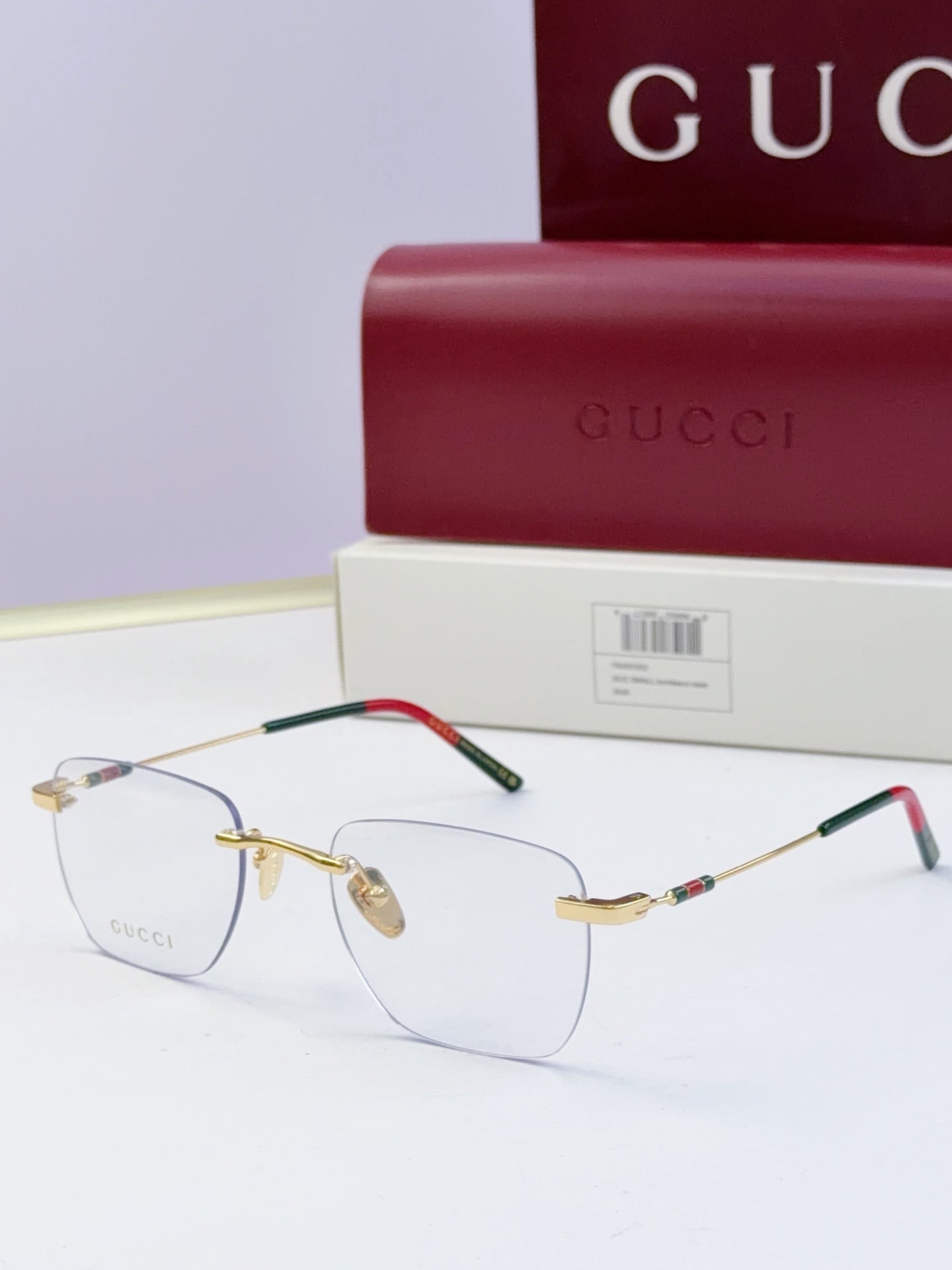 Gucci eyeglasses with clear lenses, gold-tone metal frame, black temples with multicolor stripe and red accent