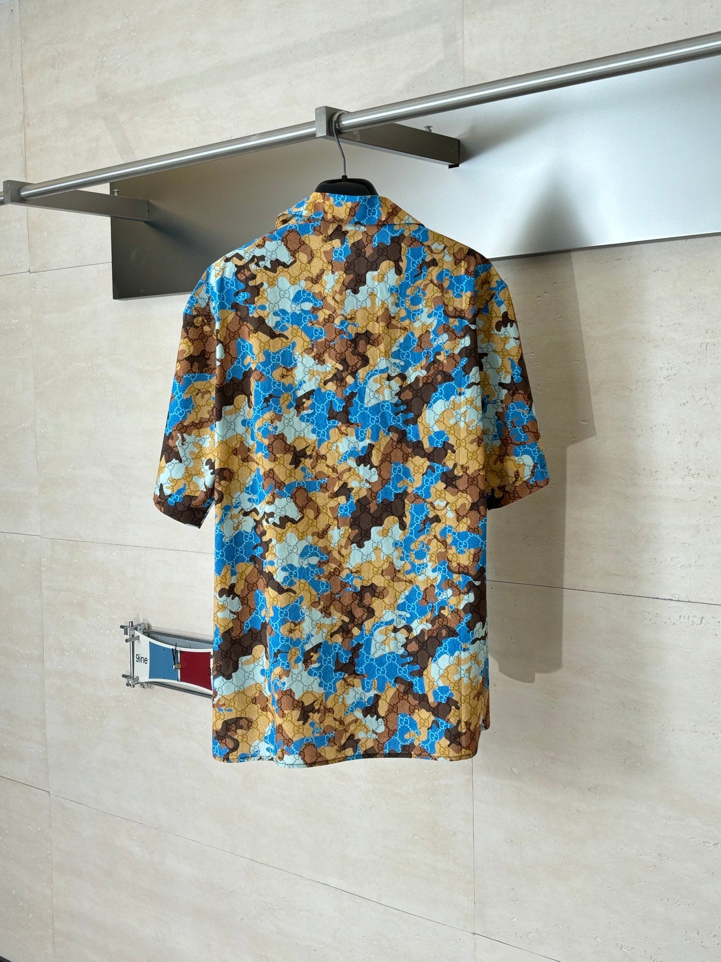 Short-sleeve button-up shirt, blue and tan abstract pattern, rear view on hanger