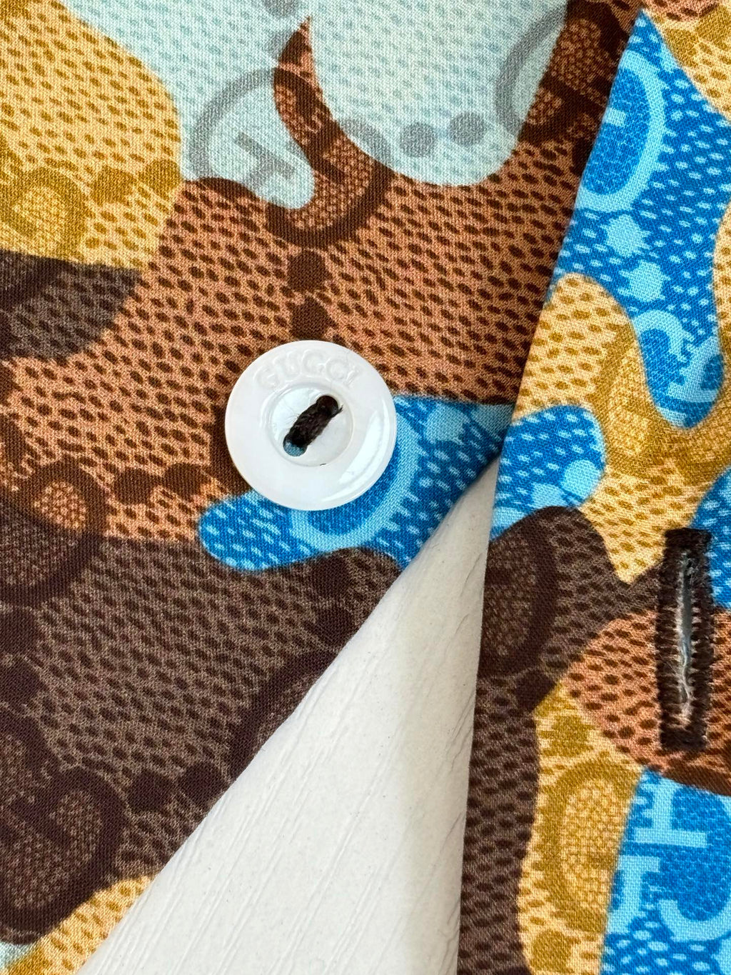Shirt button close-up with white button and blue tan brown abstract fabric