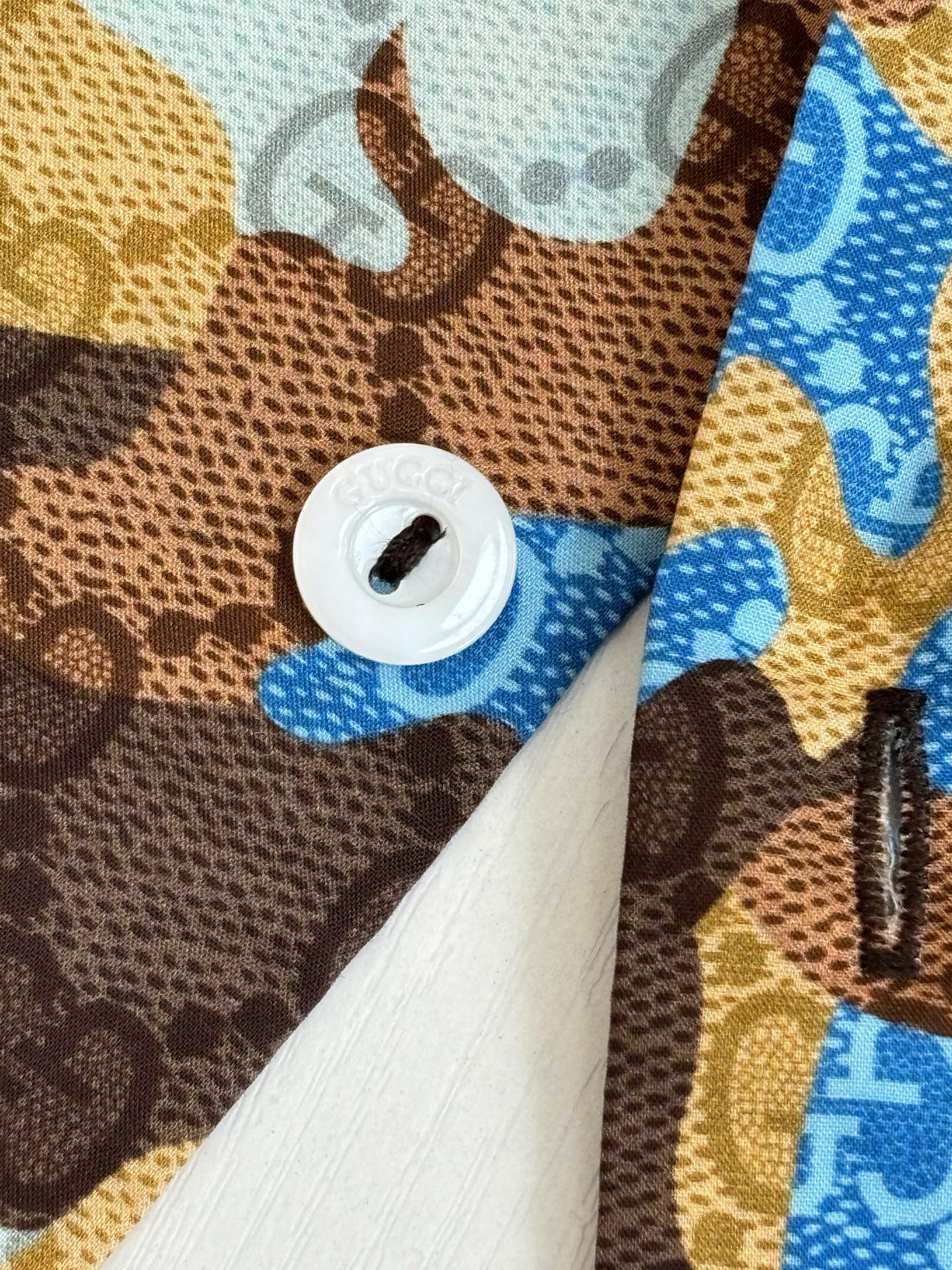 Shirt button close-up with white button and blue tan brown abstract fabric