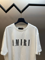 White crewneck T-shirt with large AMIRI logo on front, hanging on black hanger.