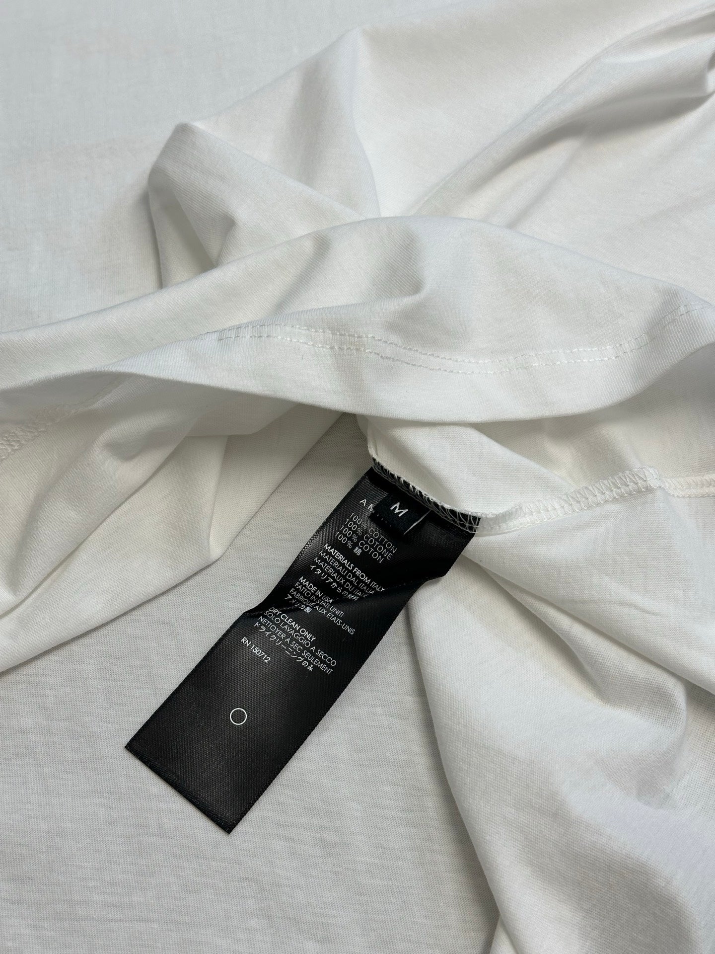 White T-shirt fabric close-up with black brand tag attached near collar.