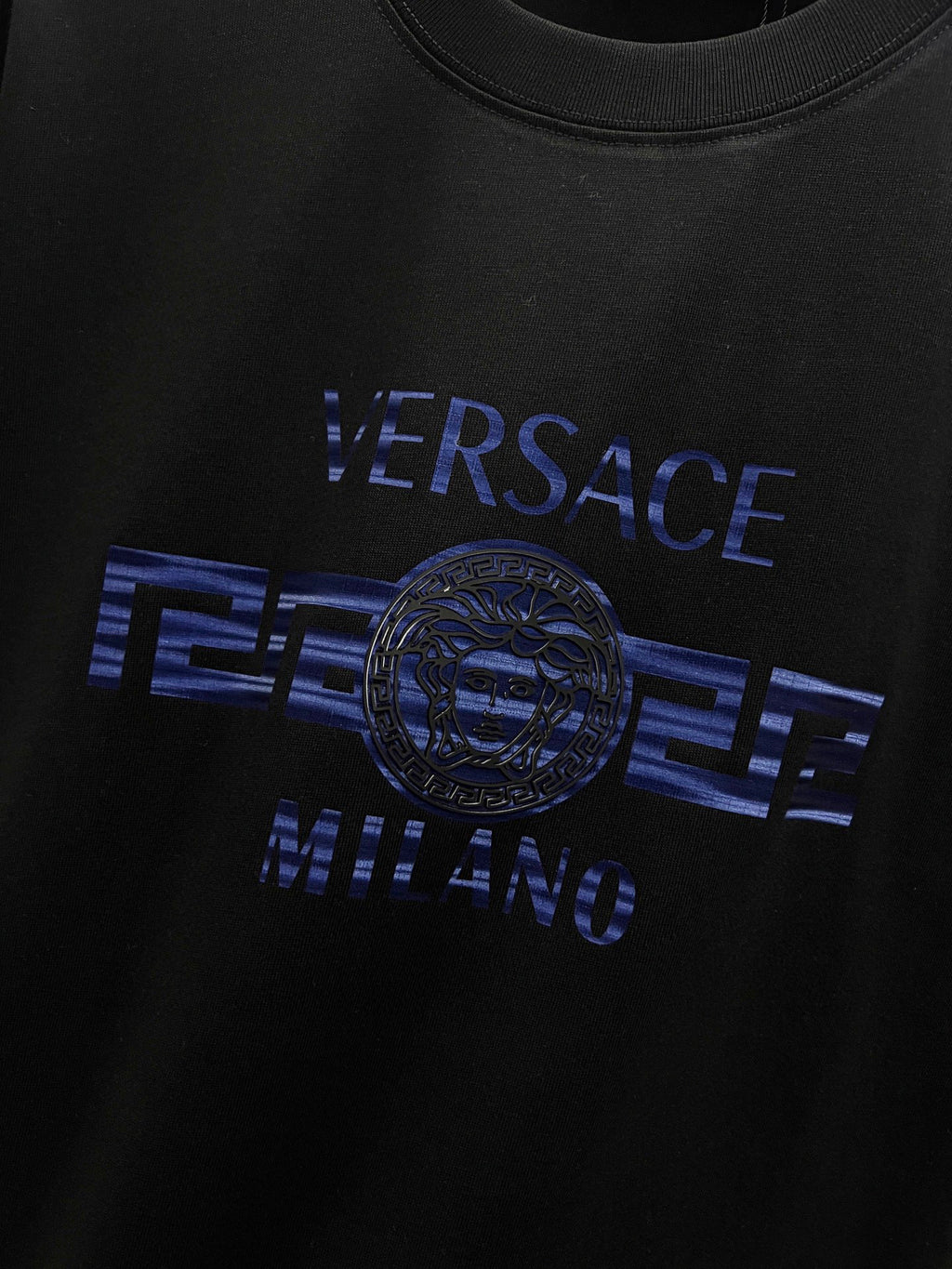 Black T-shirt close-up of blue 'VERSACE MILANO' and medallion