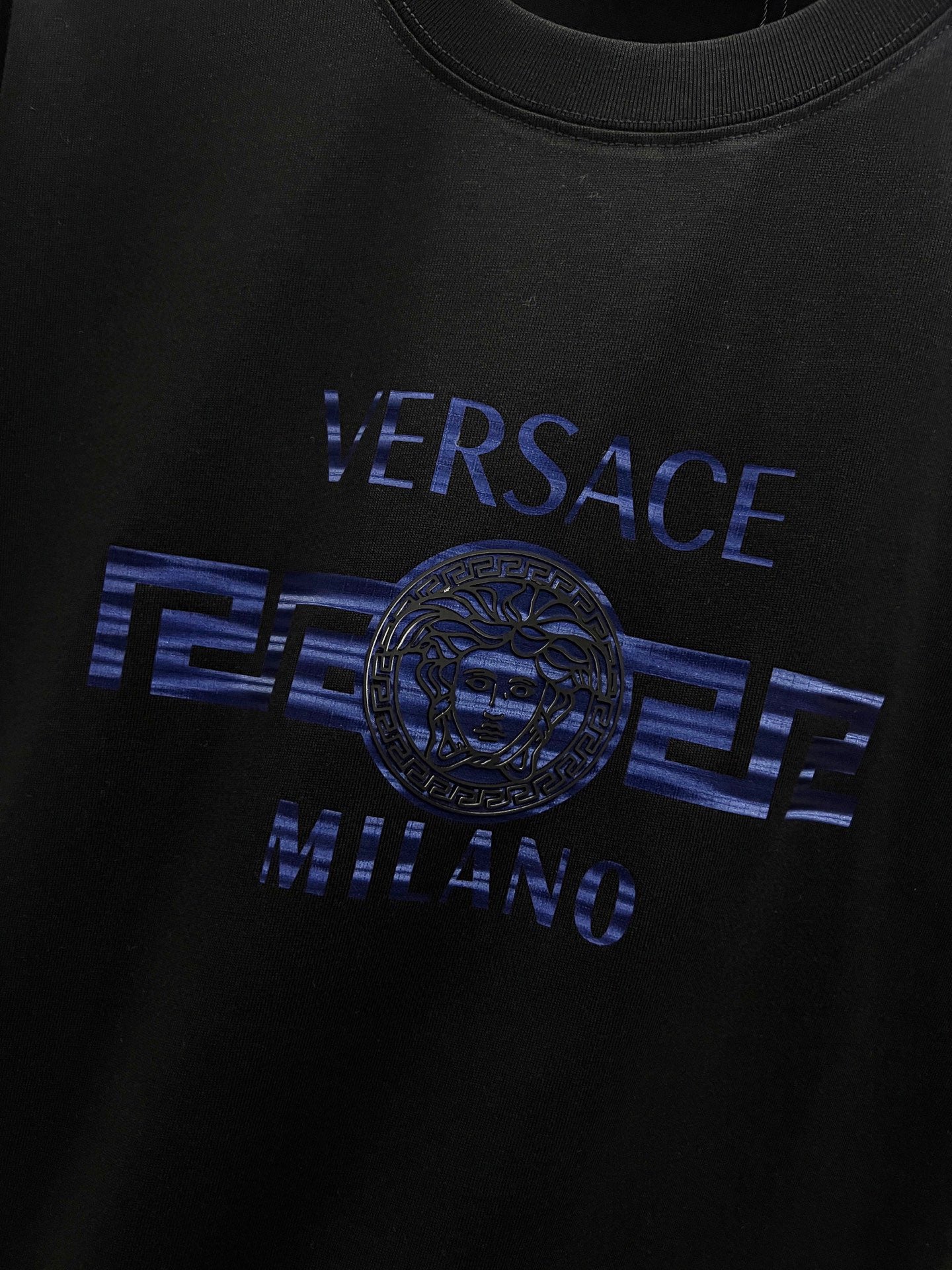 Black T-shirt close-up of blue 'VERSACE MILANO' and medallion
