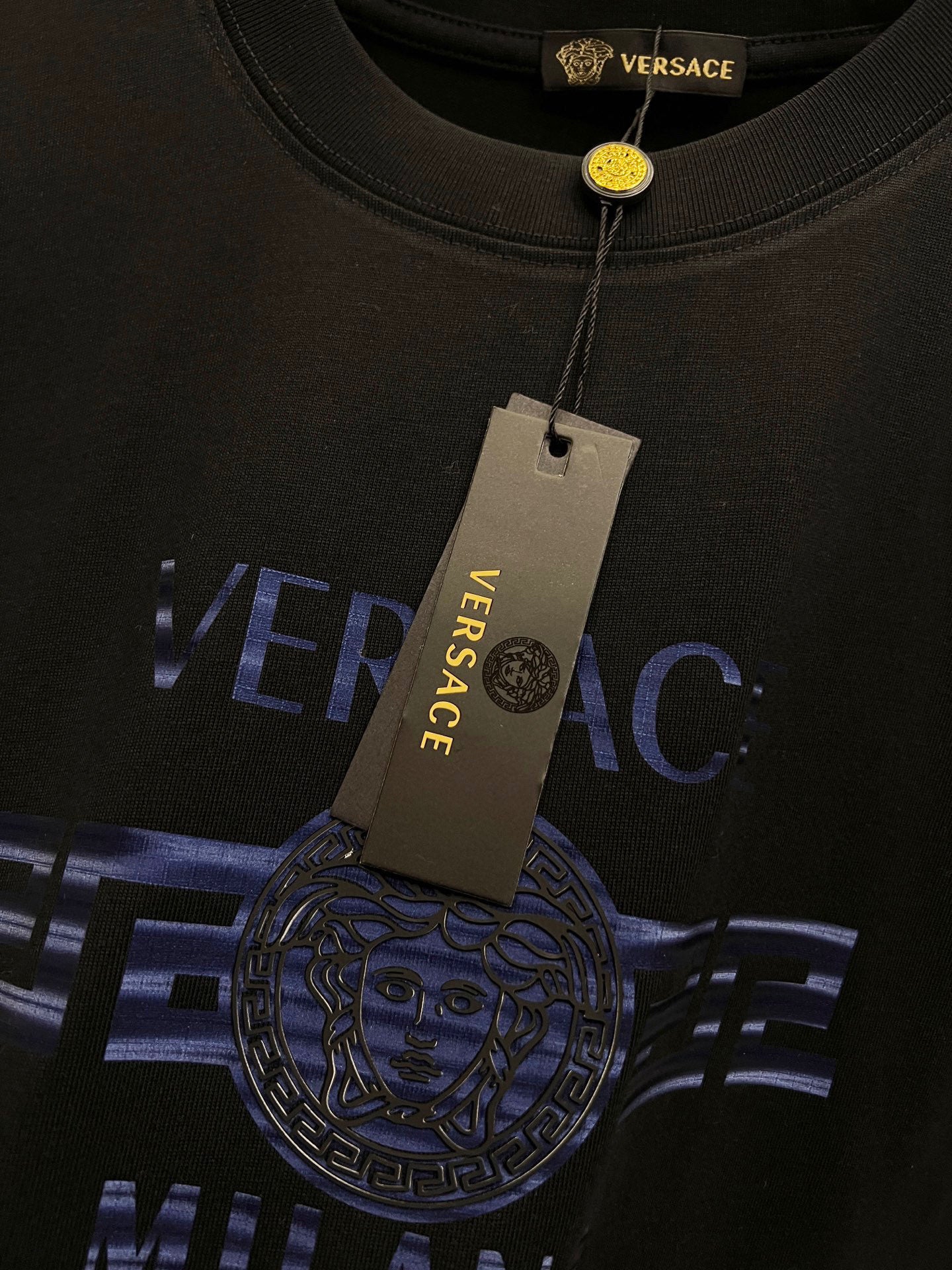 Black T-shirt close-up with blue 'VERSACE' print and round medallion