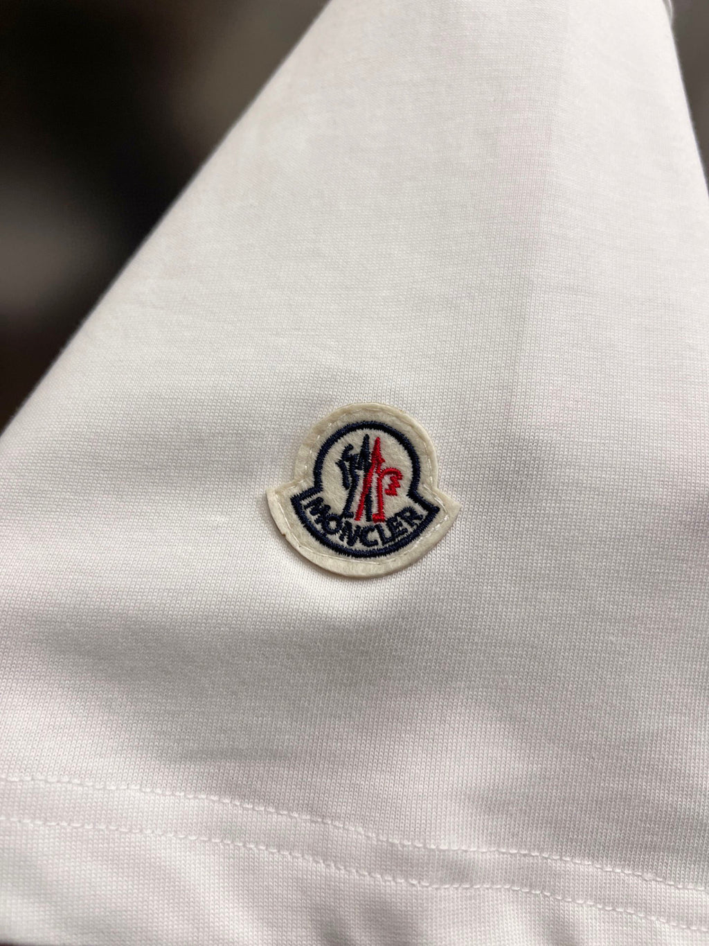 White T-shirt fabric with circular embroidered logo patch near sleeve hem