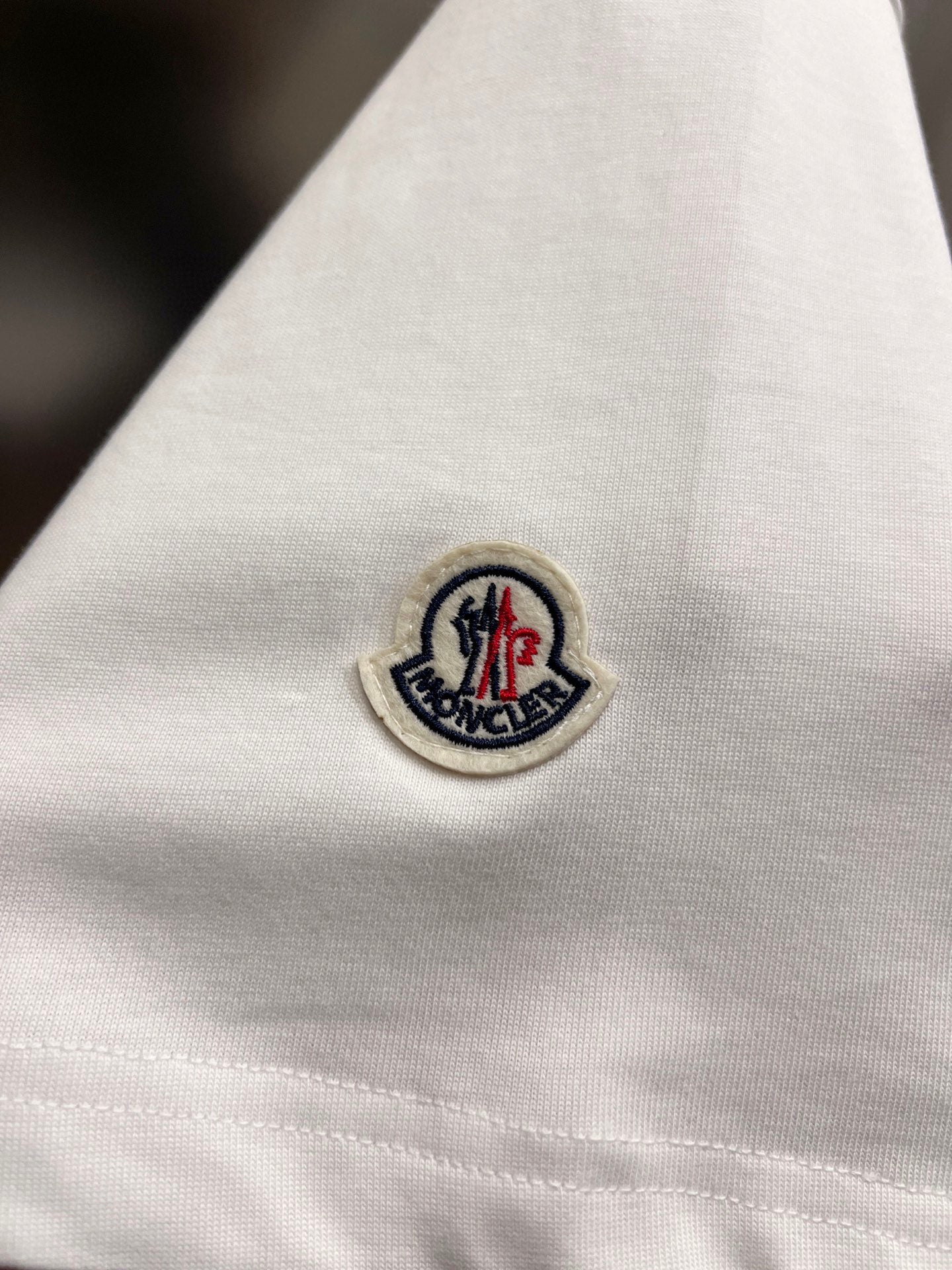 White T-shirt fabric with circular embroidered logo patch near sleeve hem