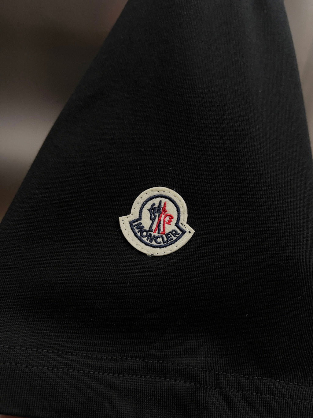 Moncler T-shirt sleeve patch, small circular logo on black knit cuff