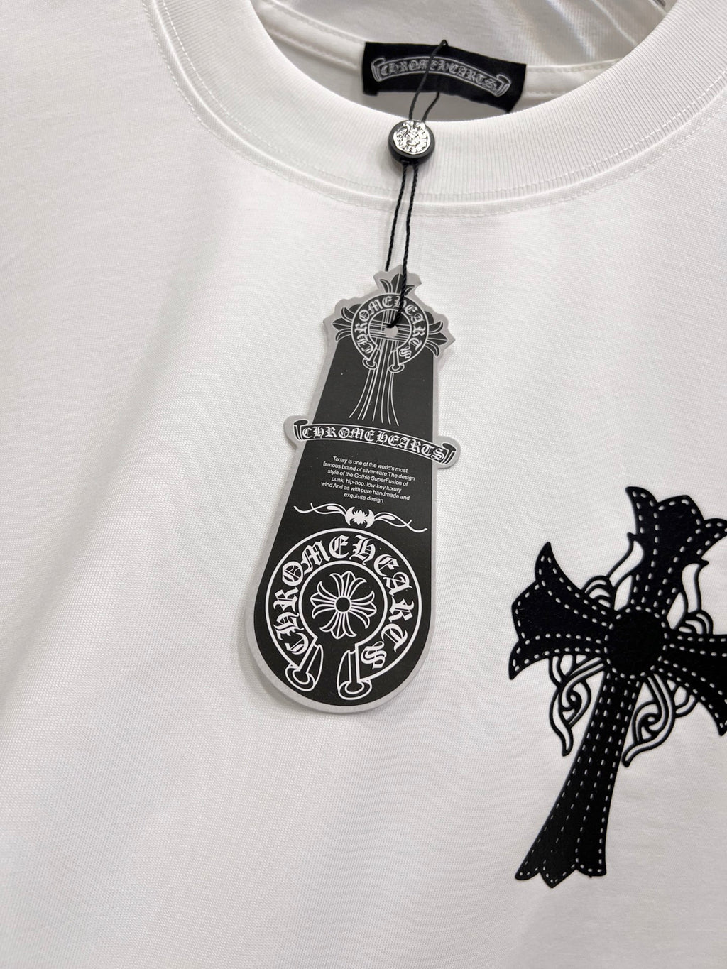 White graphic T-shirt chest close-up with black cross patch and tag-style emblem