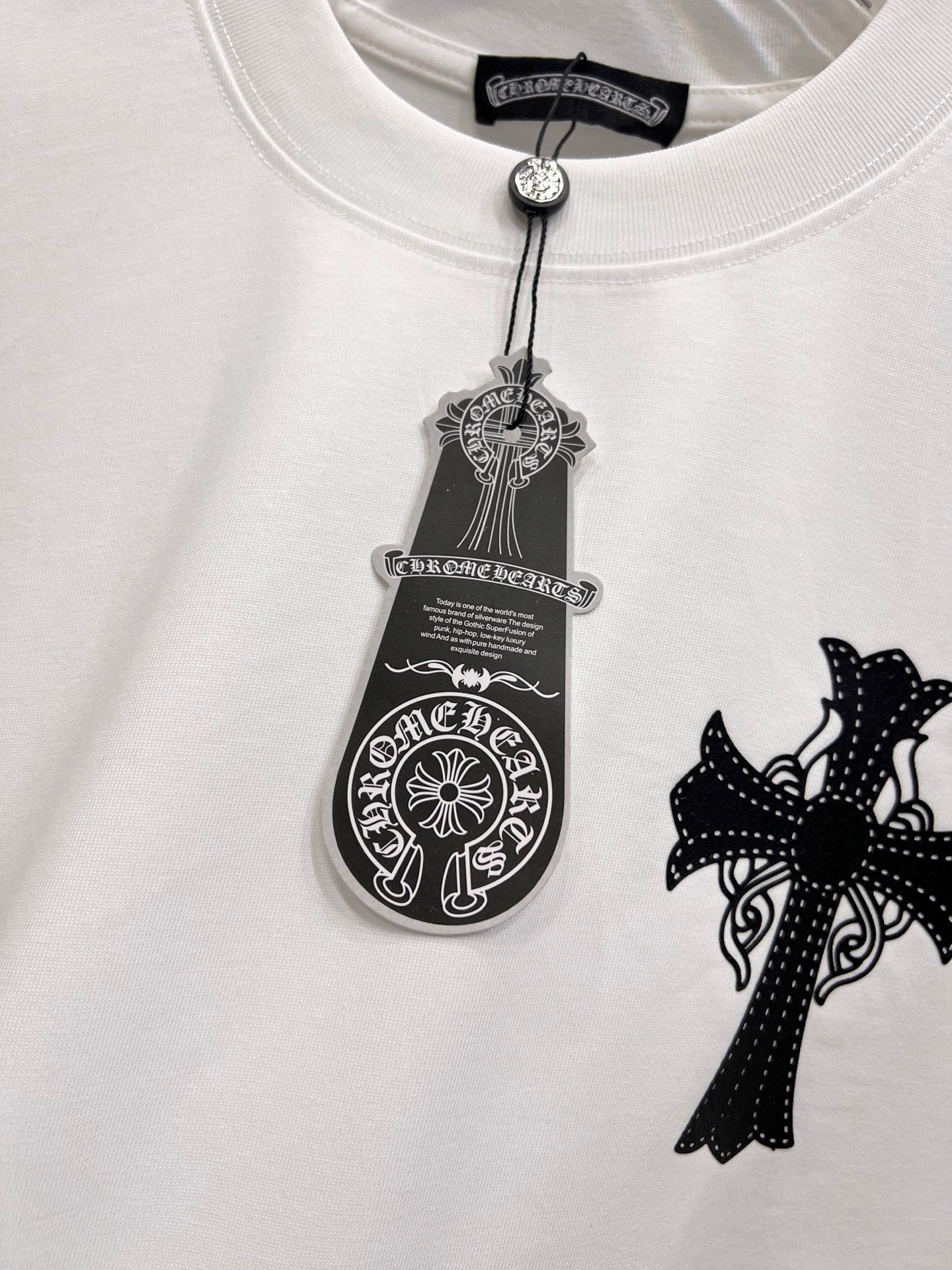 White graphic T-shirt chest close-up with black cross patch and tag-style emblem