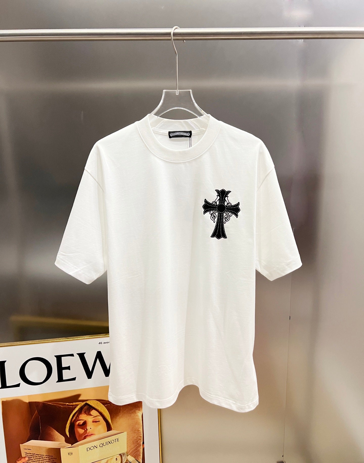 White graphic T-shirt, front view with one black cross appliqué at the chest