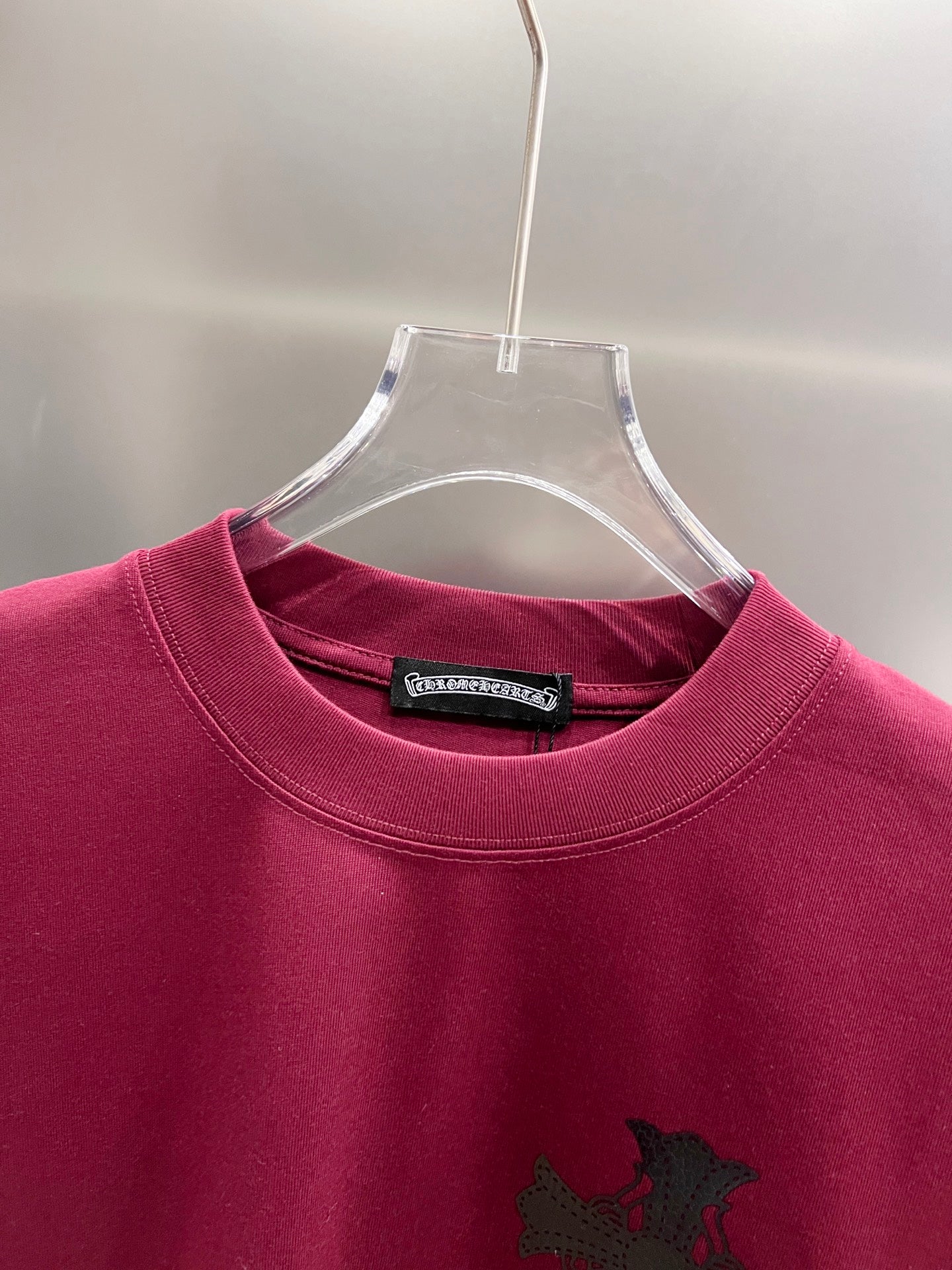 Burgundy short-sleeve T-shirt neckline with black cross graphic and interior tag.