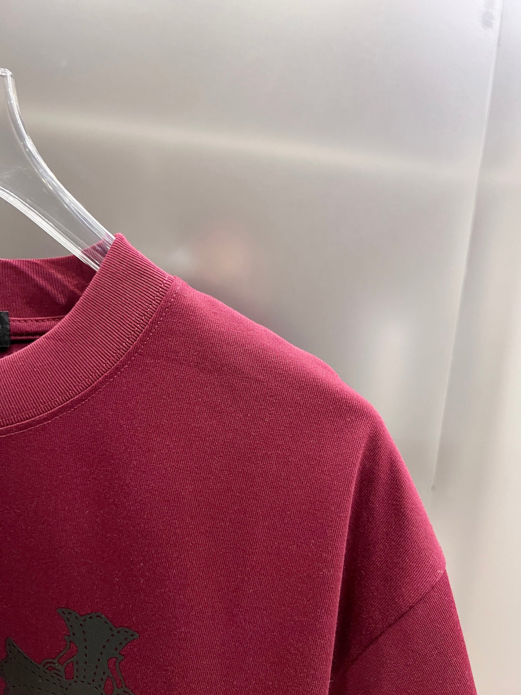Burgundy short-sleeve T-shirt shoulder and sleeve with partial black cross graphic.