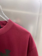 Burgundy short-sleeve T-shirt shoulder and sleeve with partial black cross graphic.