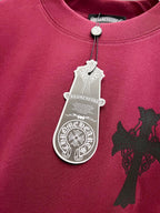 Burgundy T-shirt with silver cross design and hanging white product tag at collar.