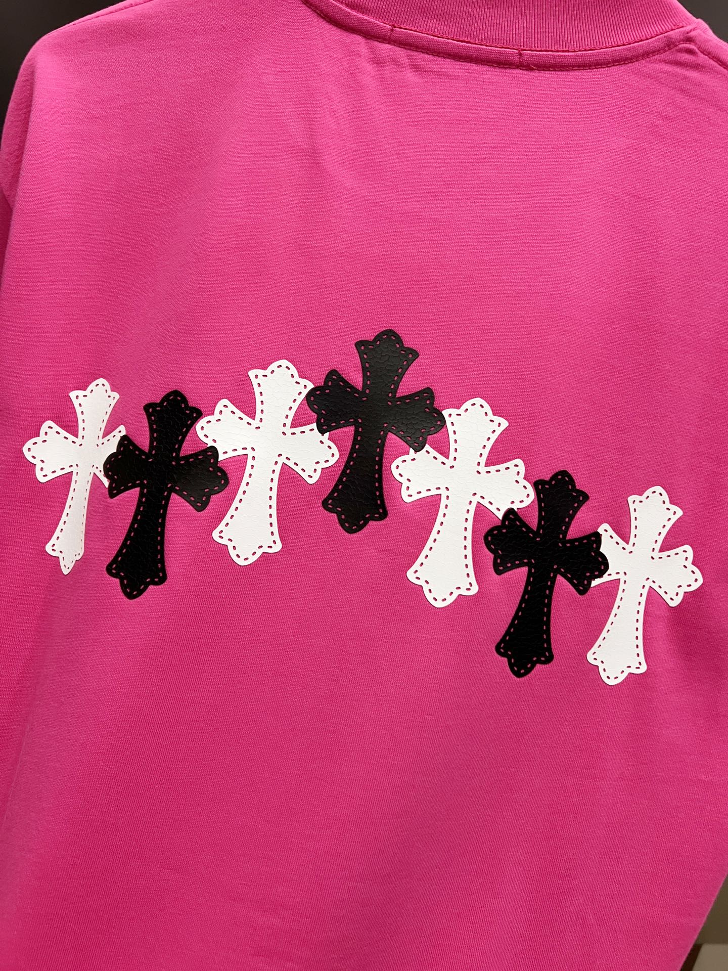 Pink short-sleeve T-shirt with row of black and white cross patches on the back