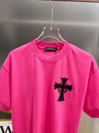 Pink short-sleeve T-shirt with small black cross graphic on the chest