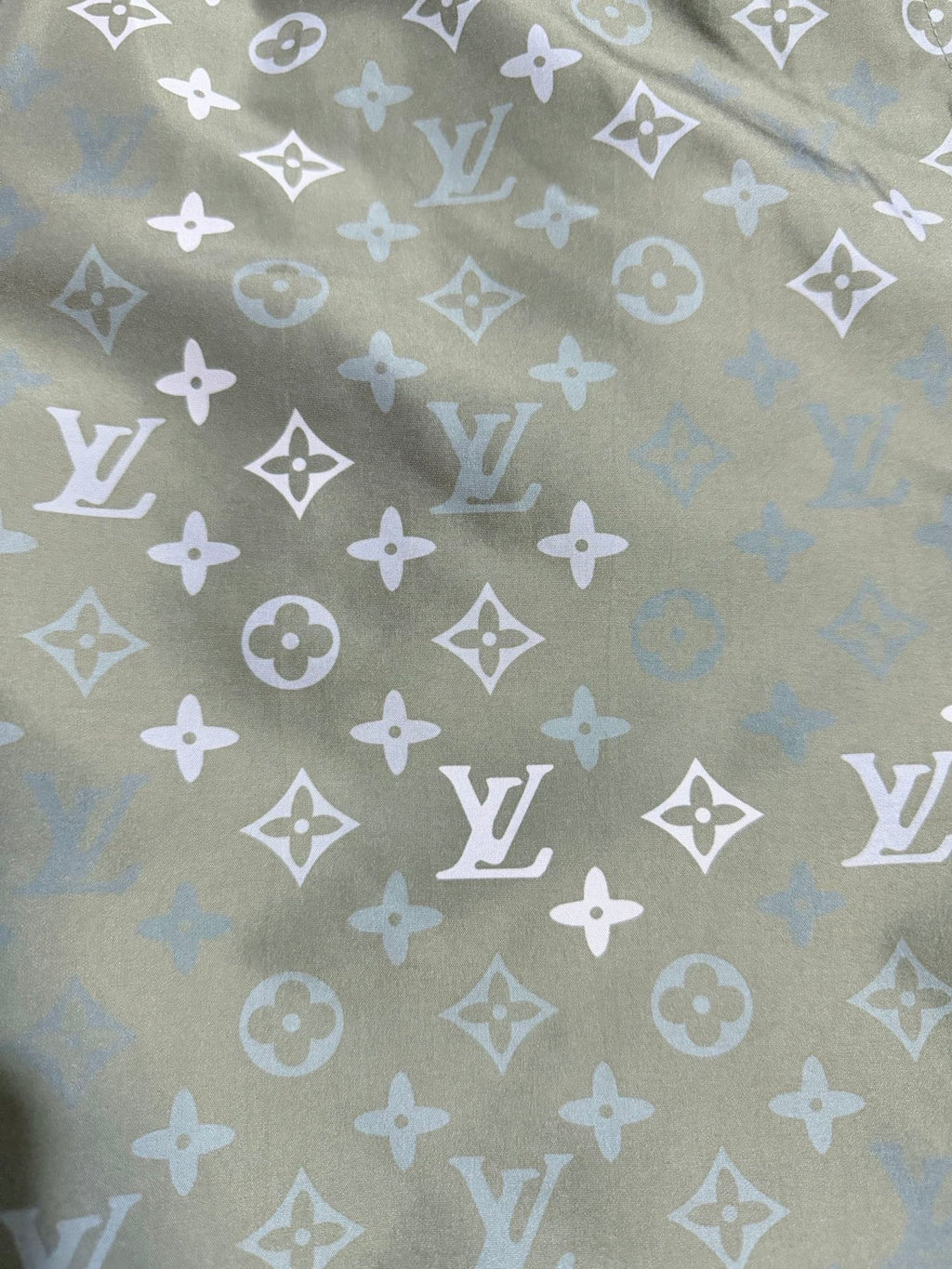 Louis Vuitton monogram fabric close-up, olive green with white repeating motifs