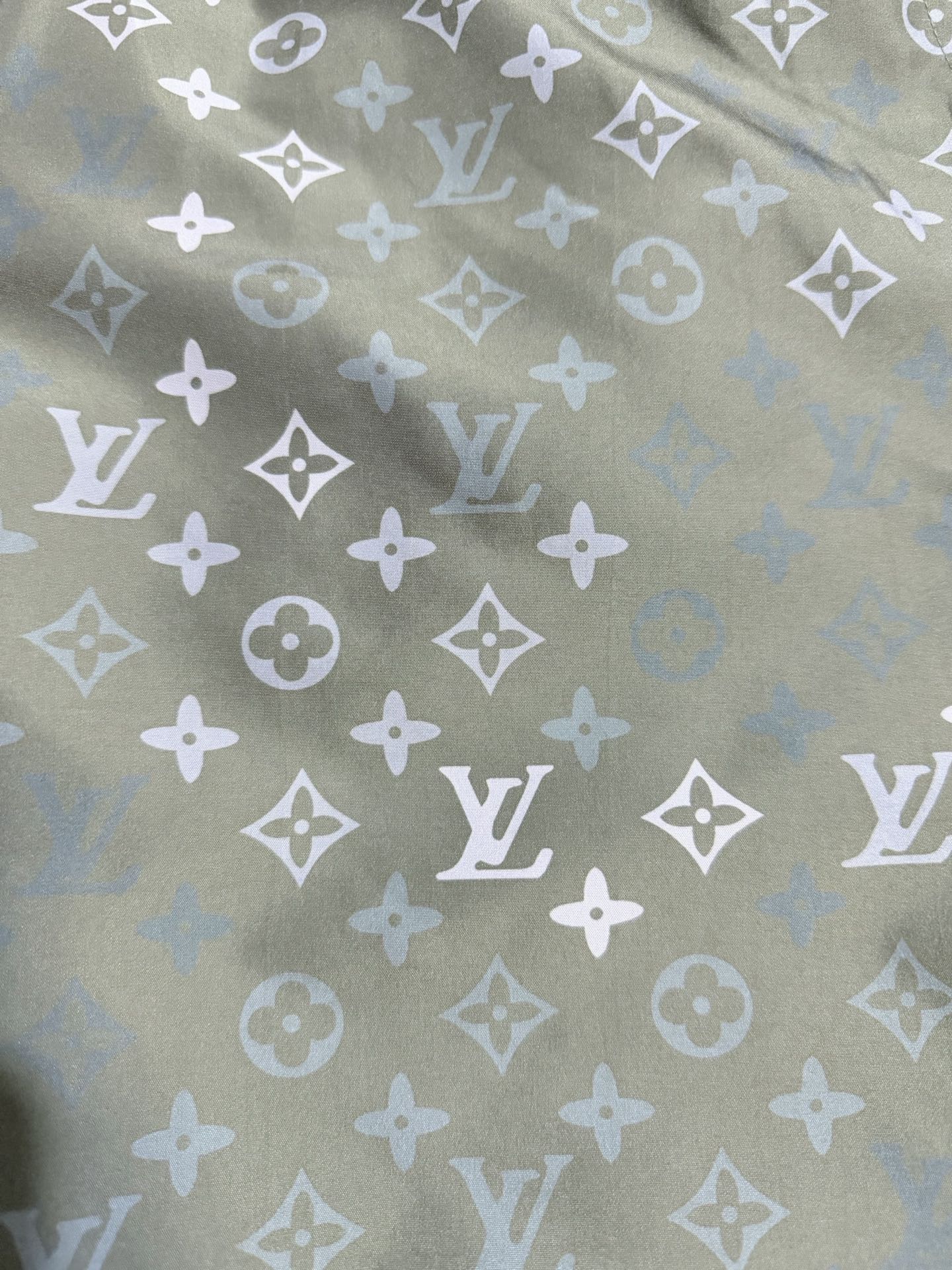 Louis Vuitton monogram fabric close-up, olive green with white repeating motifs