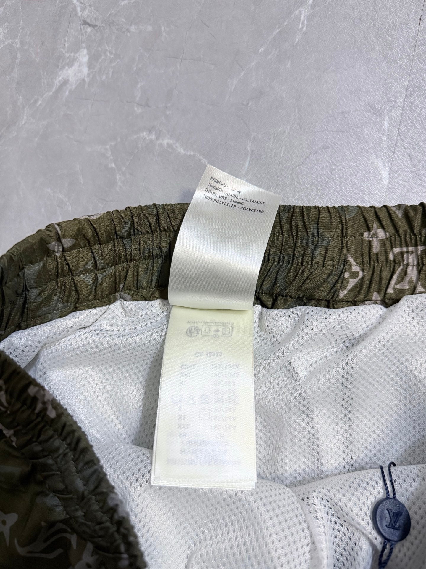 Louis Vuitton shorts with care label over white mesh lining and olive elastic waistband