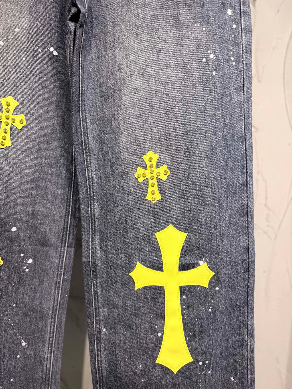 Dark gray denim pants leg with large yellow cross patch and small crosses