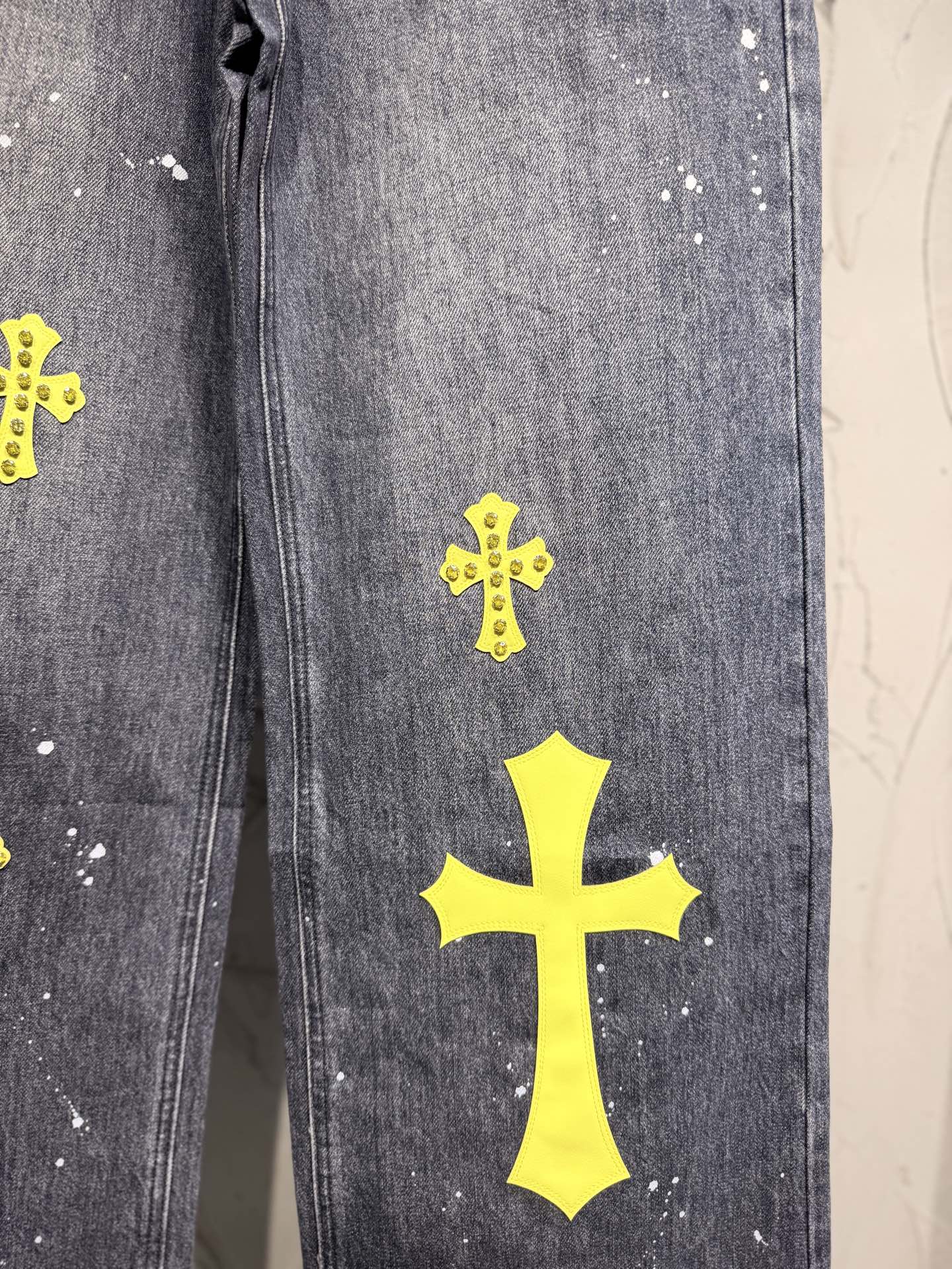 Dark gray denim pants leg with large yellow cross patch and small crosses