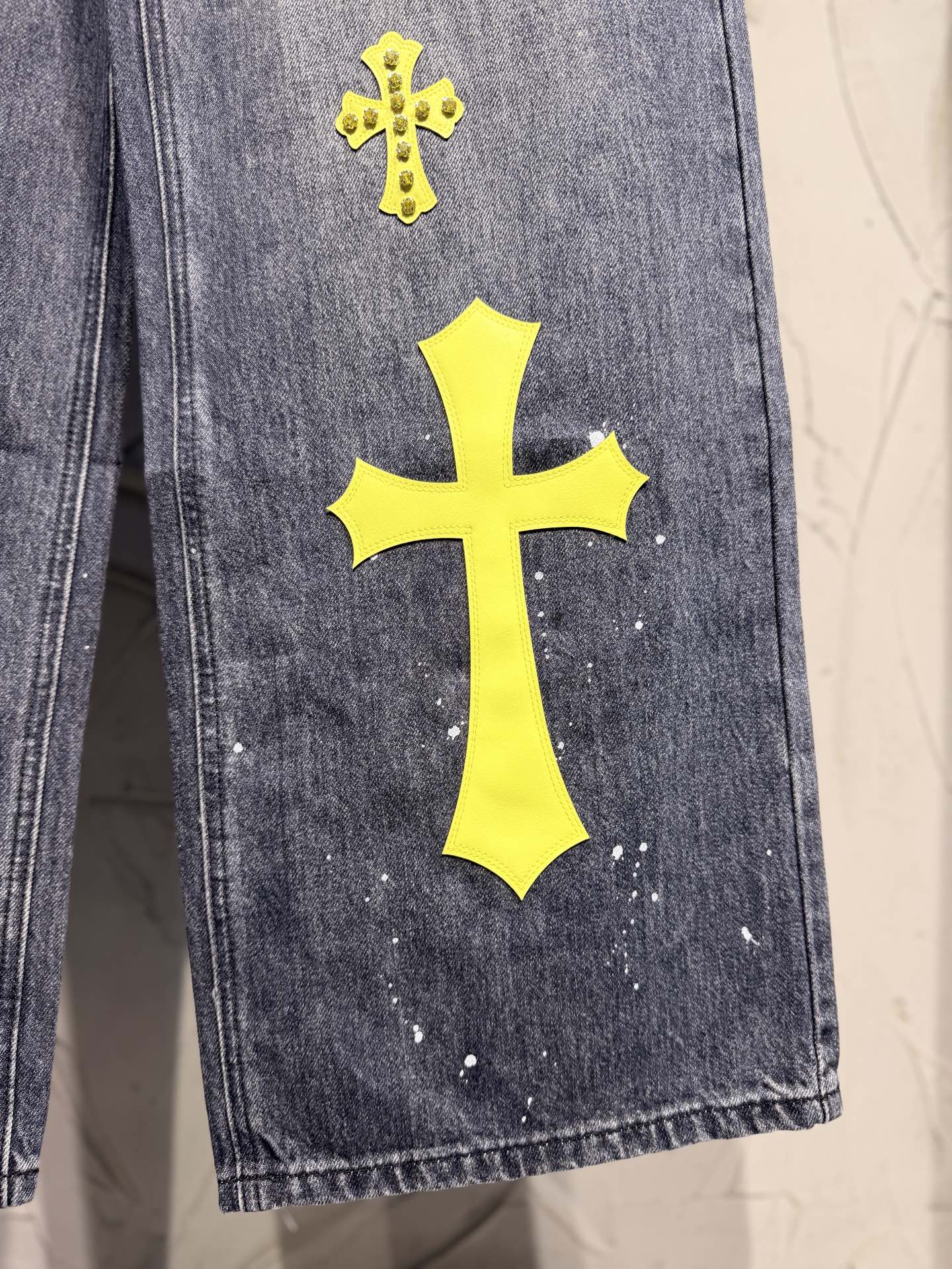 Dark gray denim pants leg with large yellow cross patch