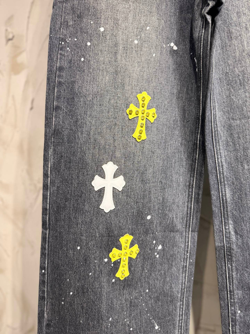 Dark gray denim pants leg with white and yellow small cross patches