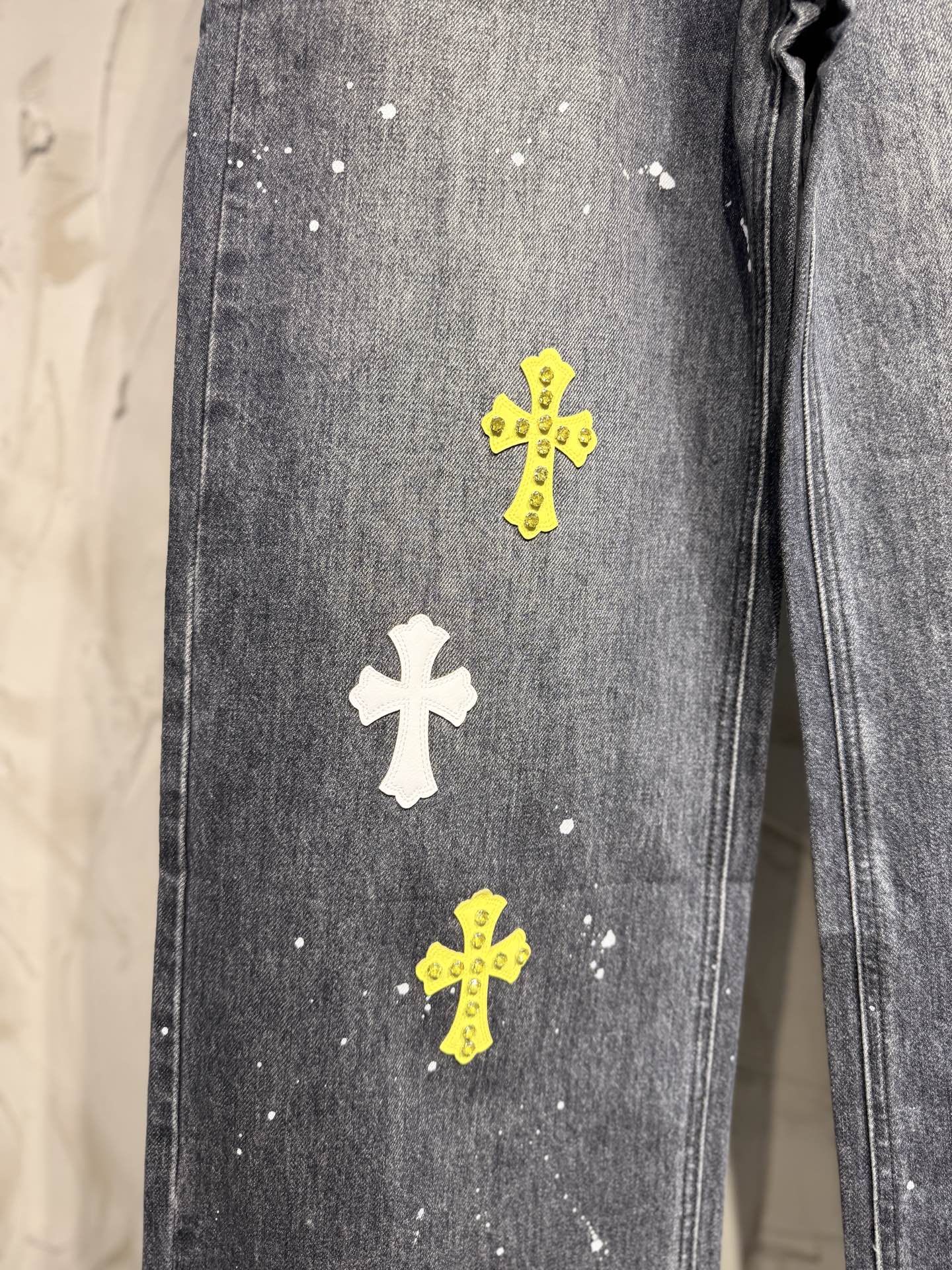 Dark gray denim pants leg with white and yellow small cross patches