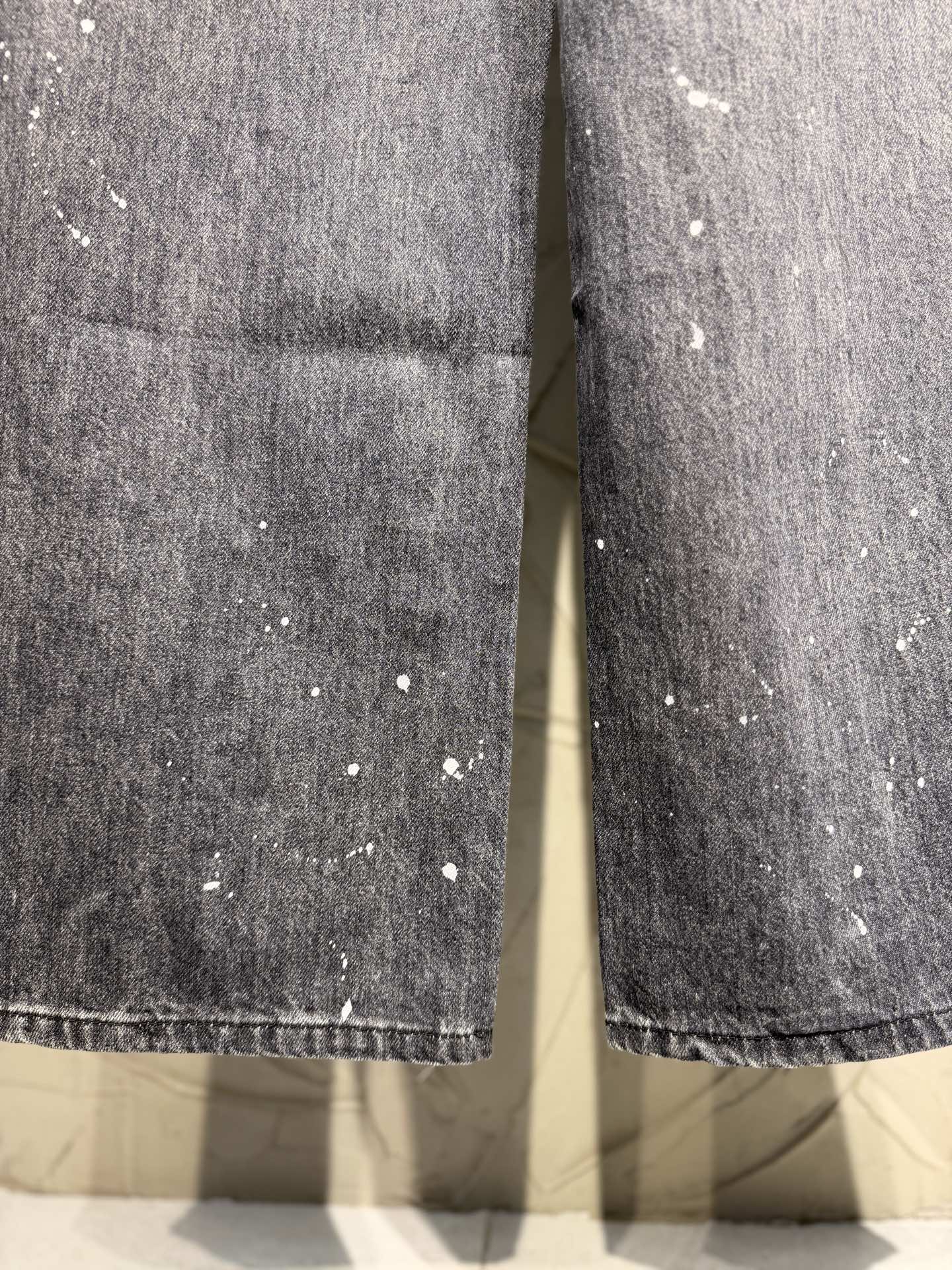 Denim pant fabric closeup with white speckled paint and stitched hem