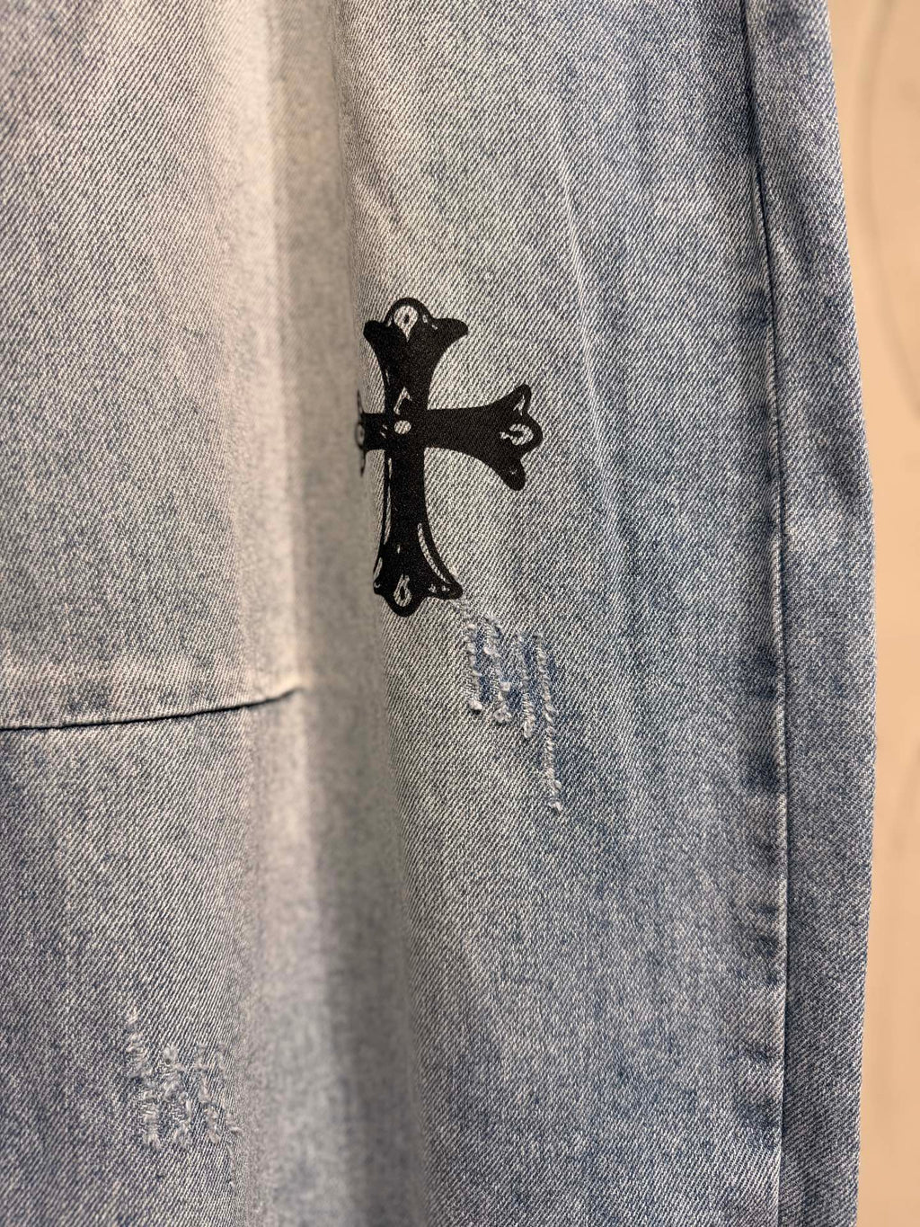 Light blue denim pants with small black cross graphic near the hem