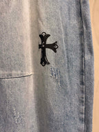 Light blue denim pants with small black cross graphic near the hem